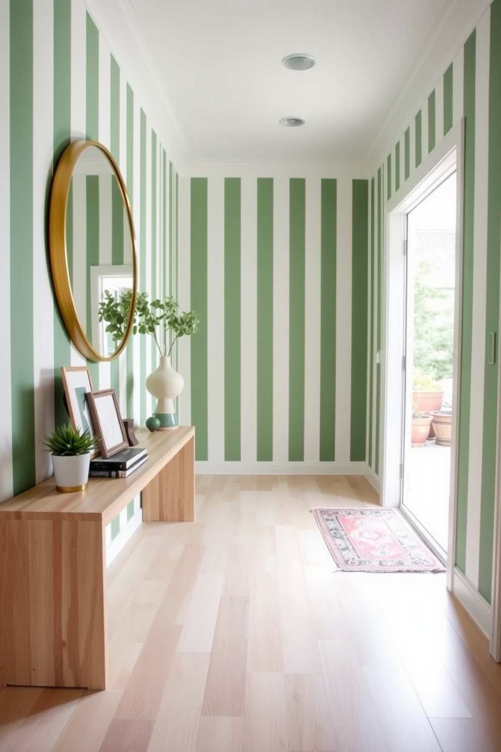 A bright and inviting foyer features green and white striped wallpaper that adds a fresh and lively touch to the space. The flooring is a light hardwood that complements the wallpaper, creating a harmonious and welcoming atmosphere. To the left, a sleek console table in a natural wood finish holds decorative items and a small potted plant. A large round mirror with a gold frame hangs above the table, reflecting the light and enhancing the sense of space.