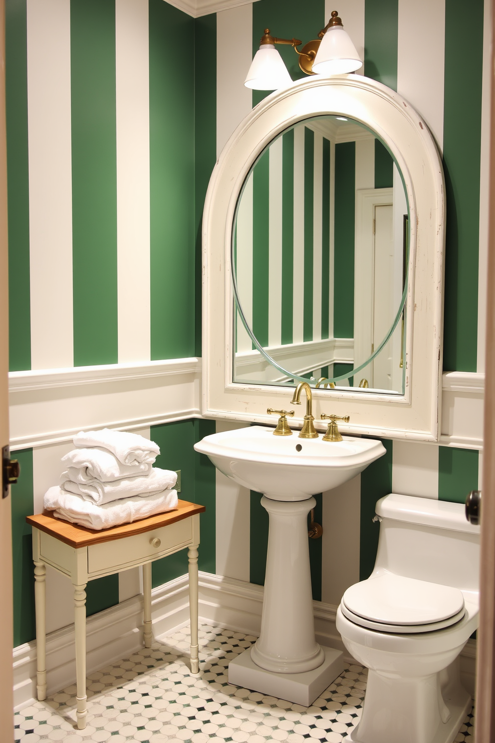 Classic green and white striped walls create an elegant atmosphere in a powder room. The room features a vintage pedestal sink with gold fixtures and a large round mirror framed in distressed white wood. A sleek white toilet is positioned next to the sink, complementing the color scheme. Soft white towels are neatly arranged on a small wooden shelf, adding a touch of warmth to the space.