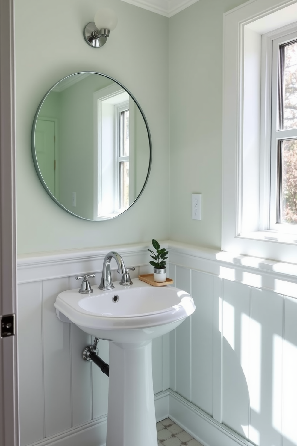 A refreshing seafoam green powder room filled with natural light. The space features a sleek pedestal sink with a polished chrome faucet and a large round mirror that enhances the brightness. Soft white wainscoting contrasts beautifully with the seafoam green walls, creating an airy feel. A small potted plant sits on a minimalist shelf, adding a touch of nature to the design.