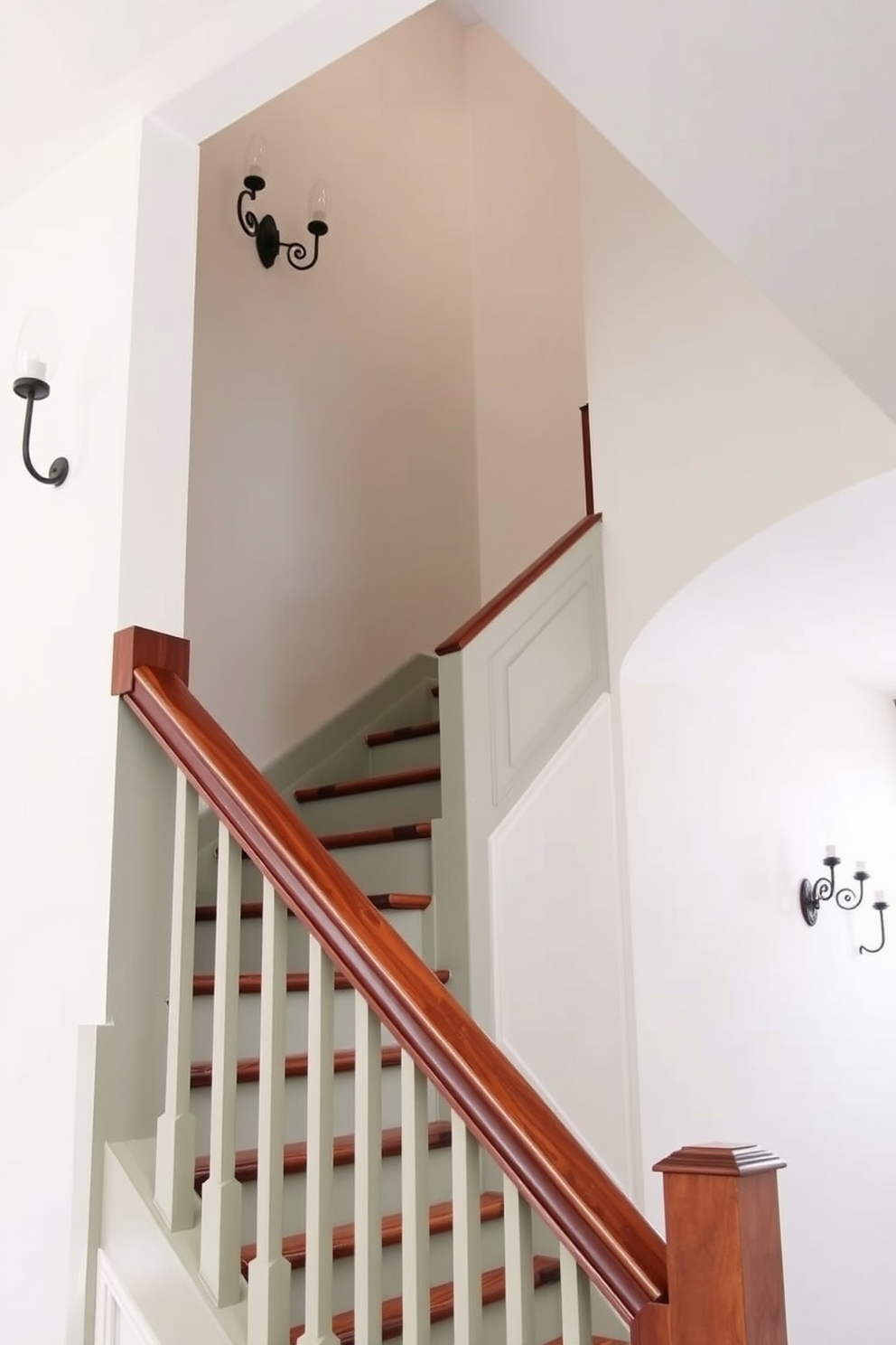 A soft sage staircase gracefully ascends, adorned with elegant fixtures that enhance its charm. The walls are painted in a complementary soft white, creating a bright and airy atmosphere around the staircase. The staircase features a sleek wooden handrail that contrasts beautifully with the sage color. Decorative wall sconces illuminate the space, casting a warm glow that highlights the staircase's refined design.