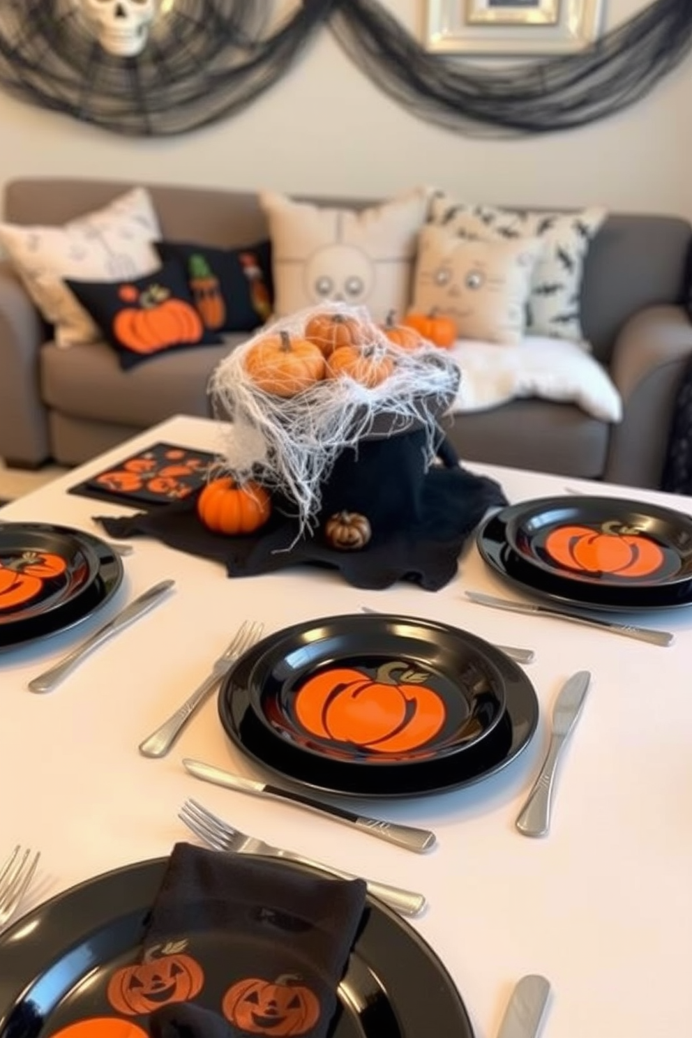 Themed tableware for Halloween dinner. The table is set with black plates adorned with orange pumpkin designs, and silver cutlery is arranged neatly beside each plate. Halloween Apartment Decorating Ideas. The living room features a cozy setup with a black and orange color scheme, including plush pillows and a spooky centerpiece made of faux cobwebs and mini pumpkins.