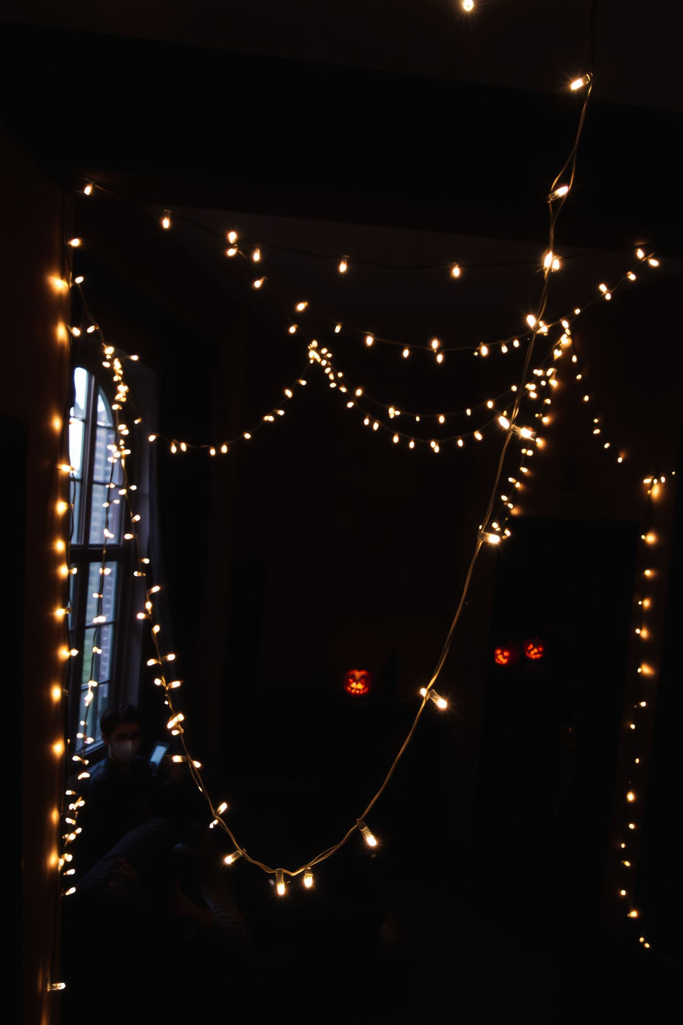 Eerie string lights are draped across the walls, casting a soft, haunting glow throughout the room. The space is adorned with dark, moody colors and Halloween-themed decorations, creating an atmosphere of spooky elegance.