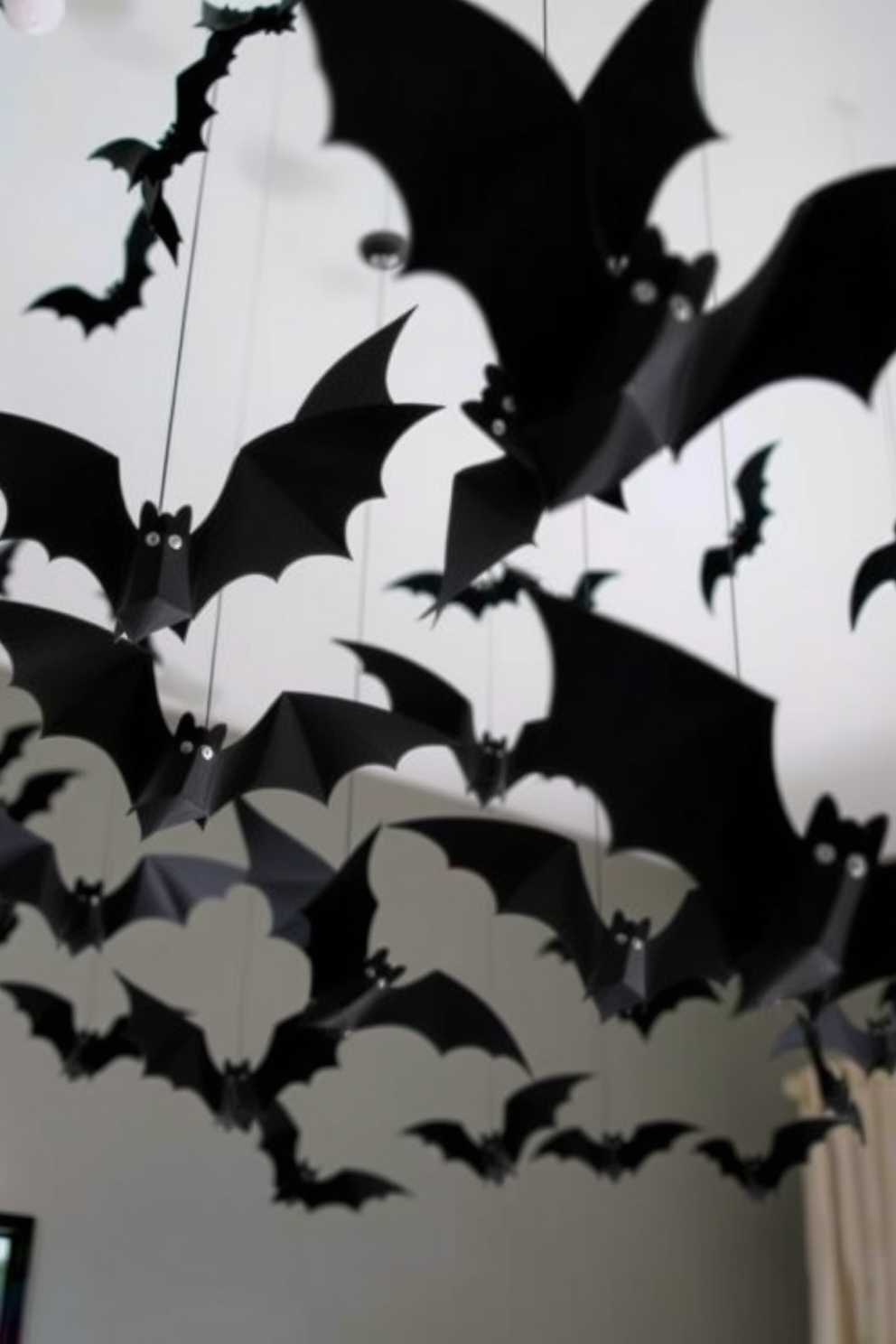 Create a spooky Halloween atmosphere with faux bats hanging from the ceiling. The bats should be in varying sizes and shapes, crafted from black paper or lightweight material, suspended at different heights to create depth and movement.