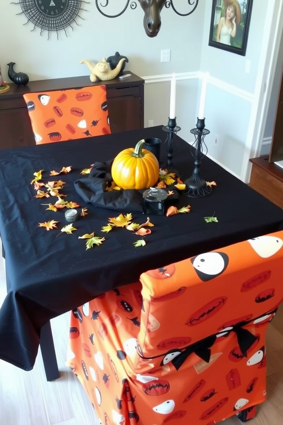 Create a cozy Halloween-themed dining room with chair covers made from orange and black fabric featuring playful pumpkin and ghost patterns. The table is set with a spooky centerpiece including a carved pumpkin, candles, and autumn leaves scattered across a dark tablecloth.