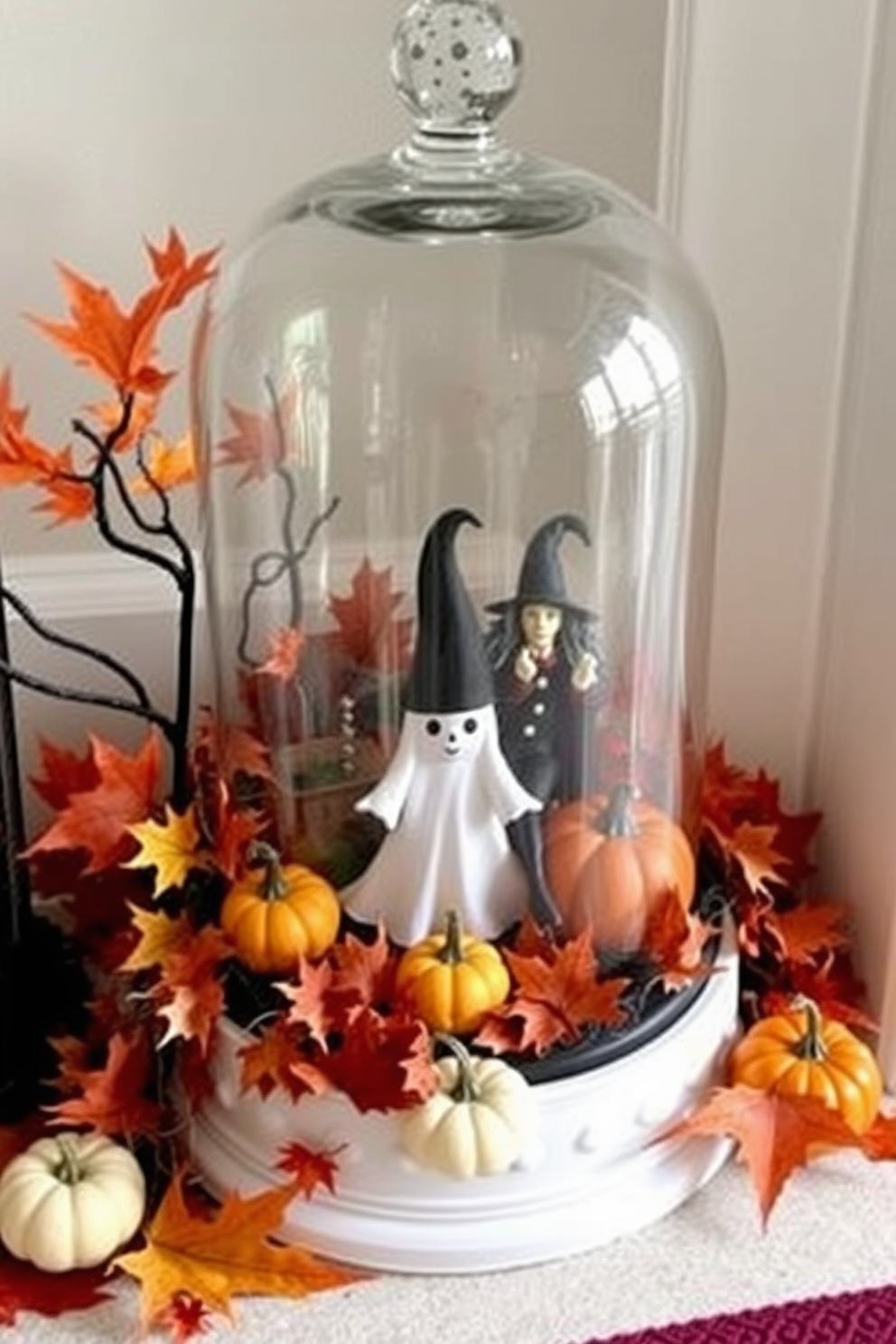 A whimsical Halloween entryway features a glass cloche filled with spooky figurines including a ghost and a witch. Surrounding the cloche are autumn leaves and small pumpkins, creating a festive and inviting atmosphere.