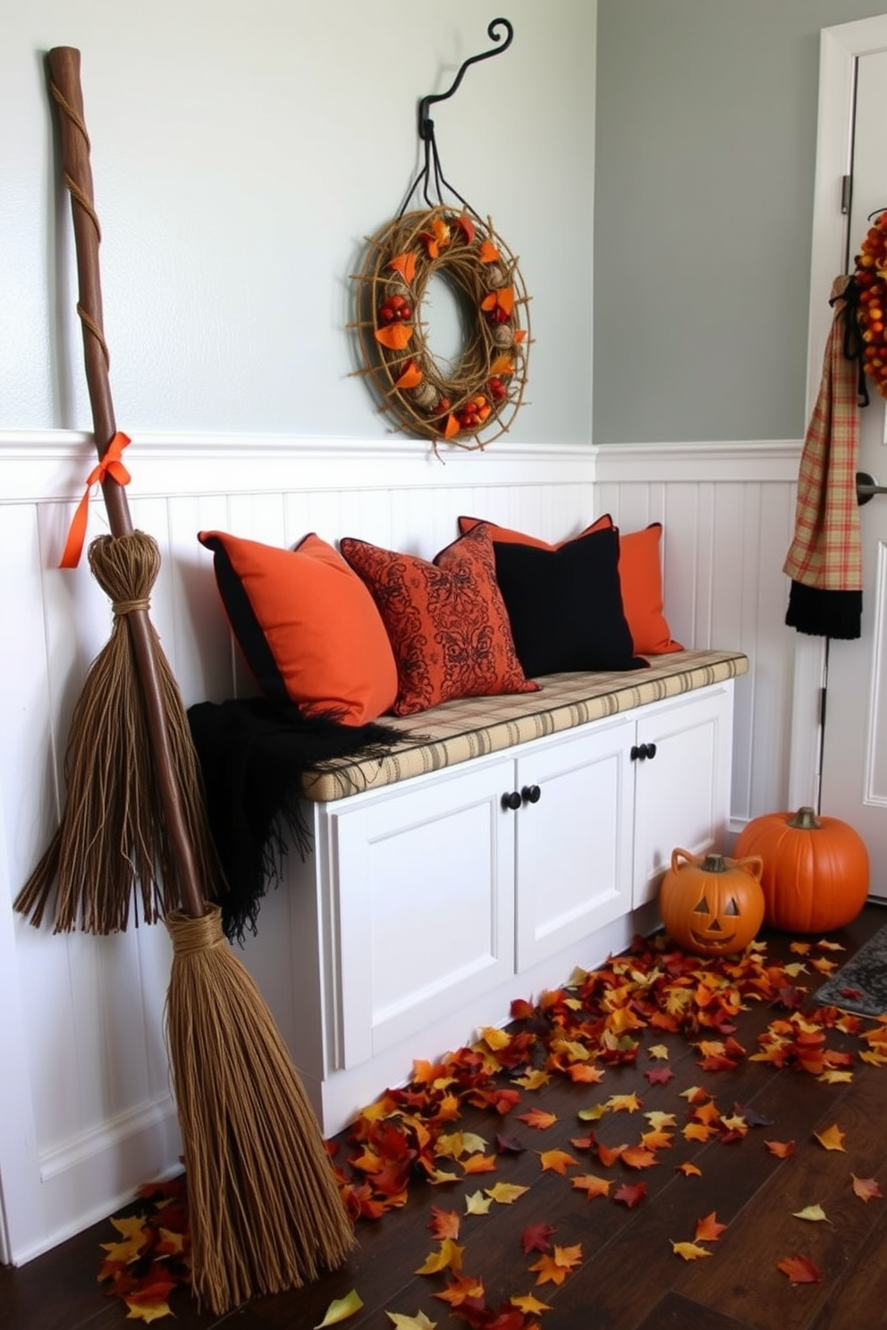 Decorative broomsticks are propped up against the wall in a festive Halloween-themed mudroom. The space features a cozy bench with orange and black throw pillows, and a collection of autumn leaves scattered on the floor.