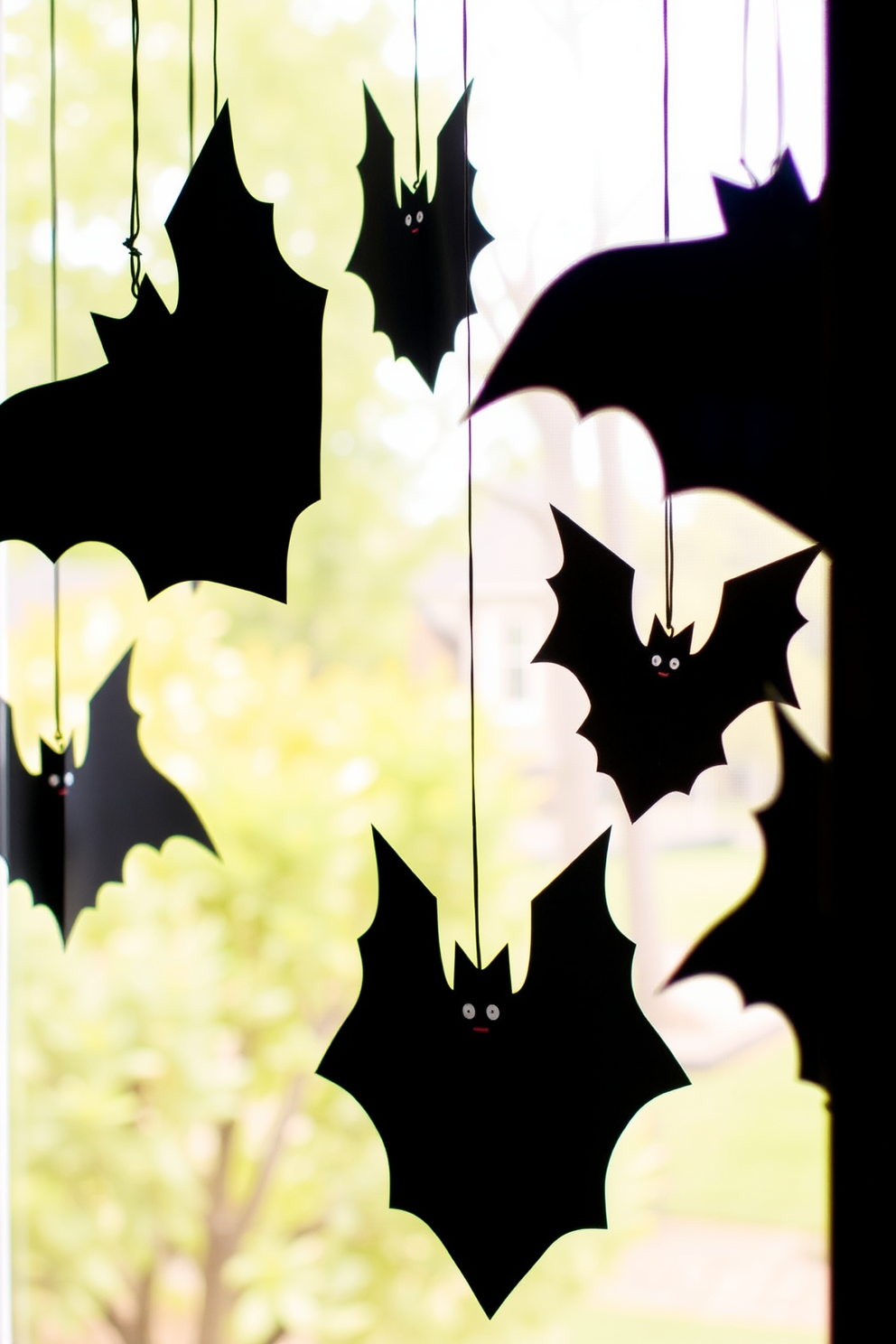 Create a spooky Halloween window display featuring hanging bats made from black cardstock. The bats should vary in size and be suspended at different heights to create a dynamic and eerie effect.