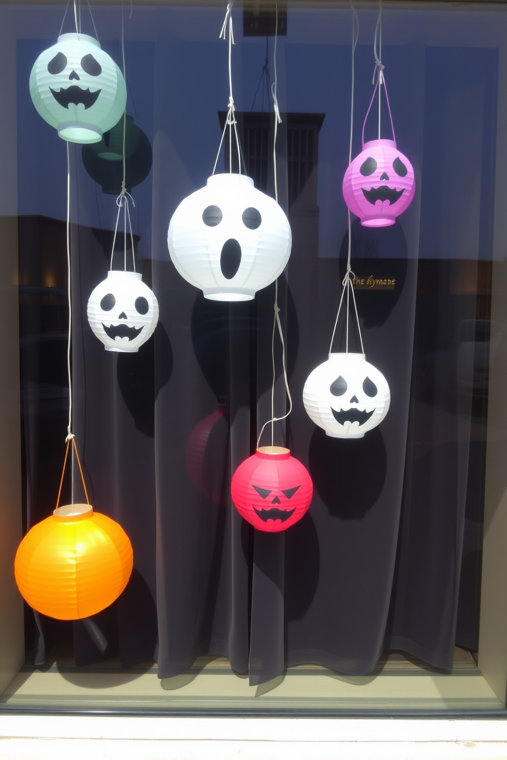 Create a whimsical Halloween window display featuring hanging paper lanterns with spooky faces. The lanterns should be in various sizes and colors, casting playful shadows on the window with a backdrop of dark, sheer curtains.