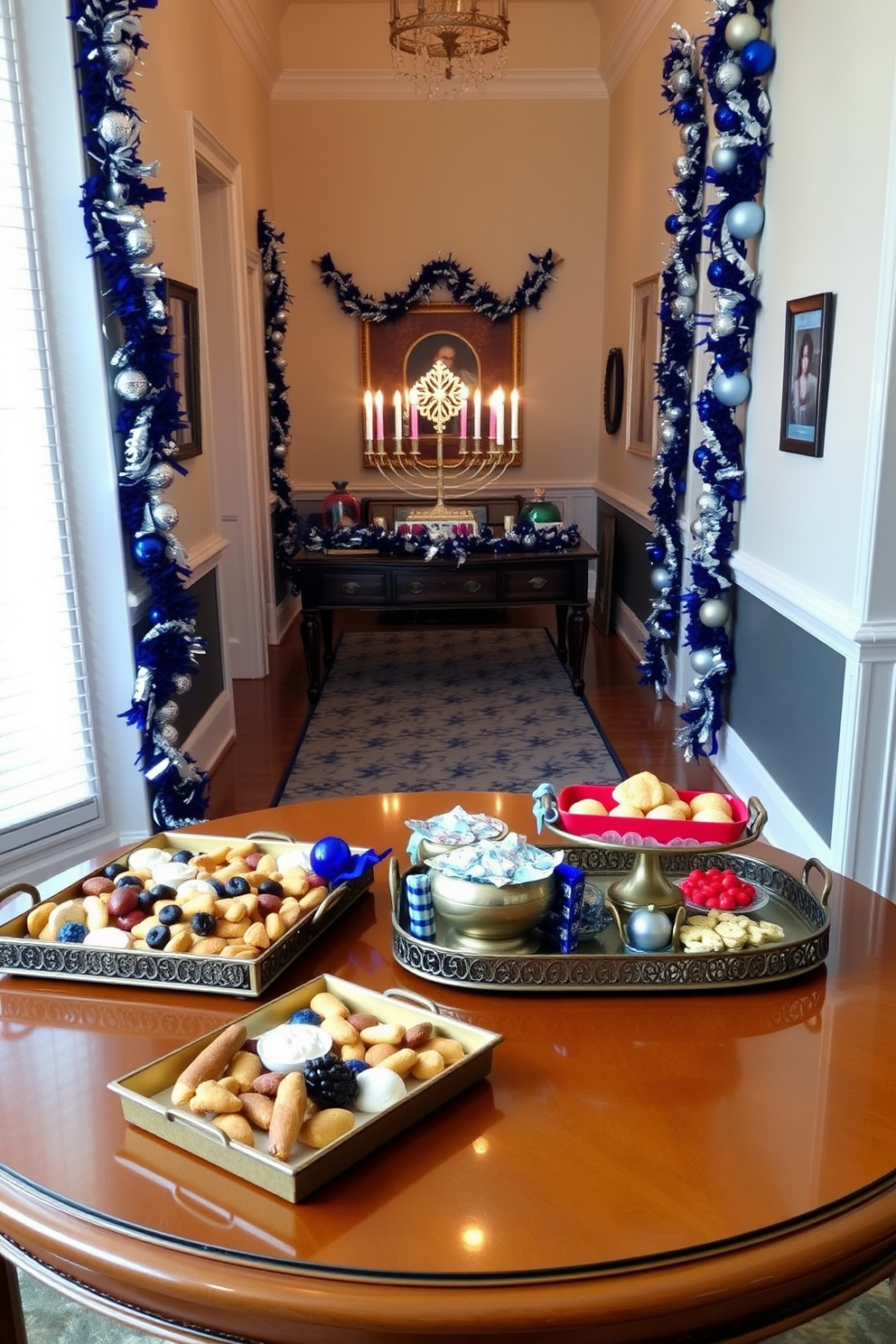 Decorative trays filled with an assortment of holiday treats are elegantly arranged on a polished wooden table. The trays feature a mix of traditional sweets and festive snacks, beautifully presented with decorative accents. The hallway is adorned with Hanukkah decorations, including blue and silver garlands draped along the walls. A menorah stands prominently on a console table, surrounded by shimmering candles and festive ornaments.