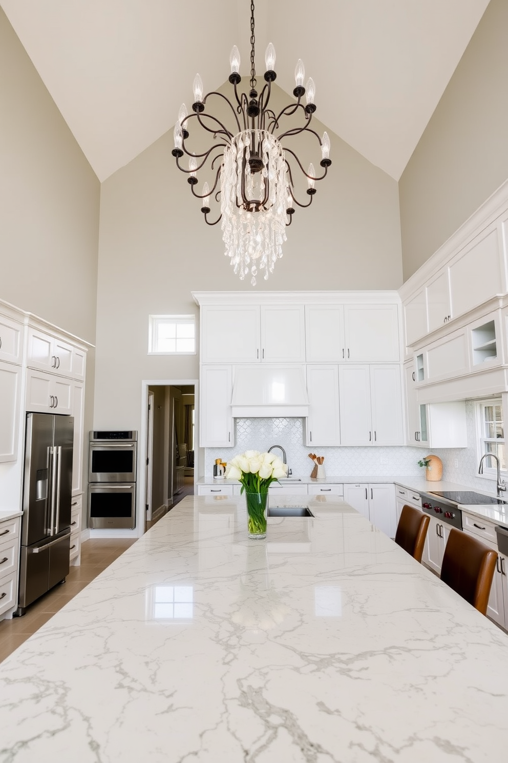 A high ceiling kitchen featuring a statement chandelier as the centerpiece. The kitchen island is made of polished granite with bar stools arranged around it, complemented by sleek cabinetry in a soft white finish.