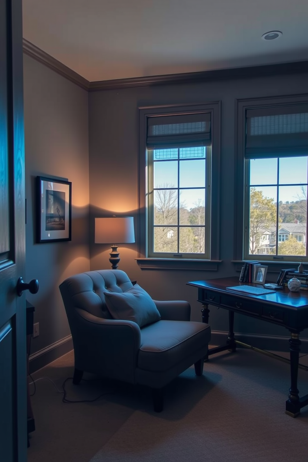 A cozy home office den features a plush lounge chair positioned near a large window, allowing natural light to fill the space. The walls are painted in a soft gray, complemented by a wooden desk that holds a stylish lamp and a few decorative books.