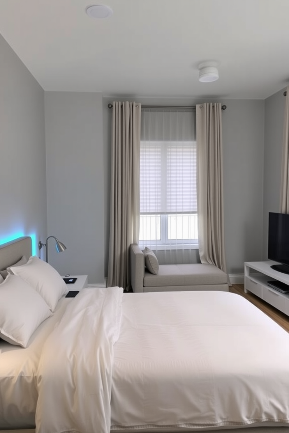 A modern in-law bedroom that incorporates smart home technology for convenience and comfort. The room features a queen-sized bed with a sleek headboard, bedside tables with wireless charging pads, and ambient lighting controlled by a smart device. The walls are painted in a calming light gray, complemented by soft blue accents in the bedding and curtains. A cozy seating area with a small sofa and a smart TV creates a welcoming space for relaxation and entertainment.