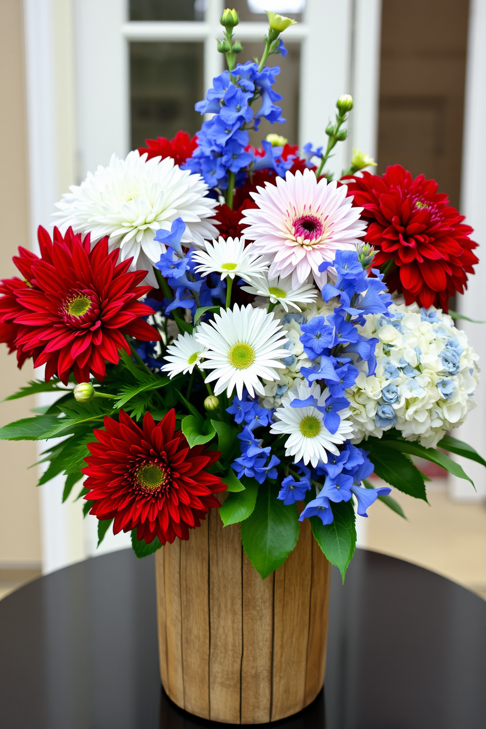 A festive display featuring red white and blue floral arrangements ideal for Independence Day celebrations. The arrangement includes vibrant dahlias and hydrangeas complemented by white daisies and blue delphiniums in a rustic wooden vase.