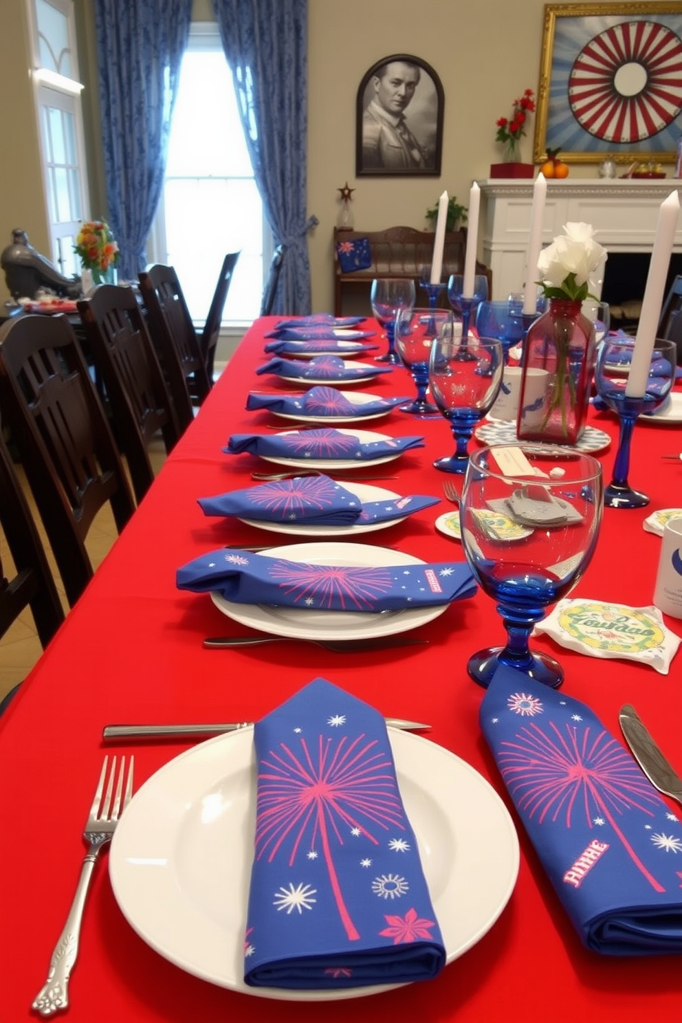 A festive dining room setting featuring firework patterned napkins laid out for guests. The table is adorned with a vibrant red tablecloth, complemented by white dishes and blue glassware to celebrate Independence Day.