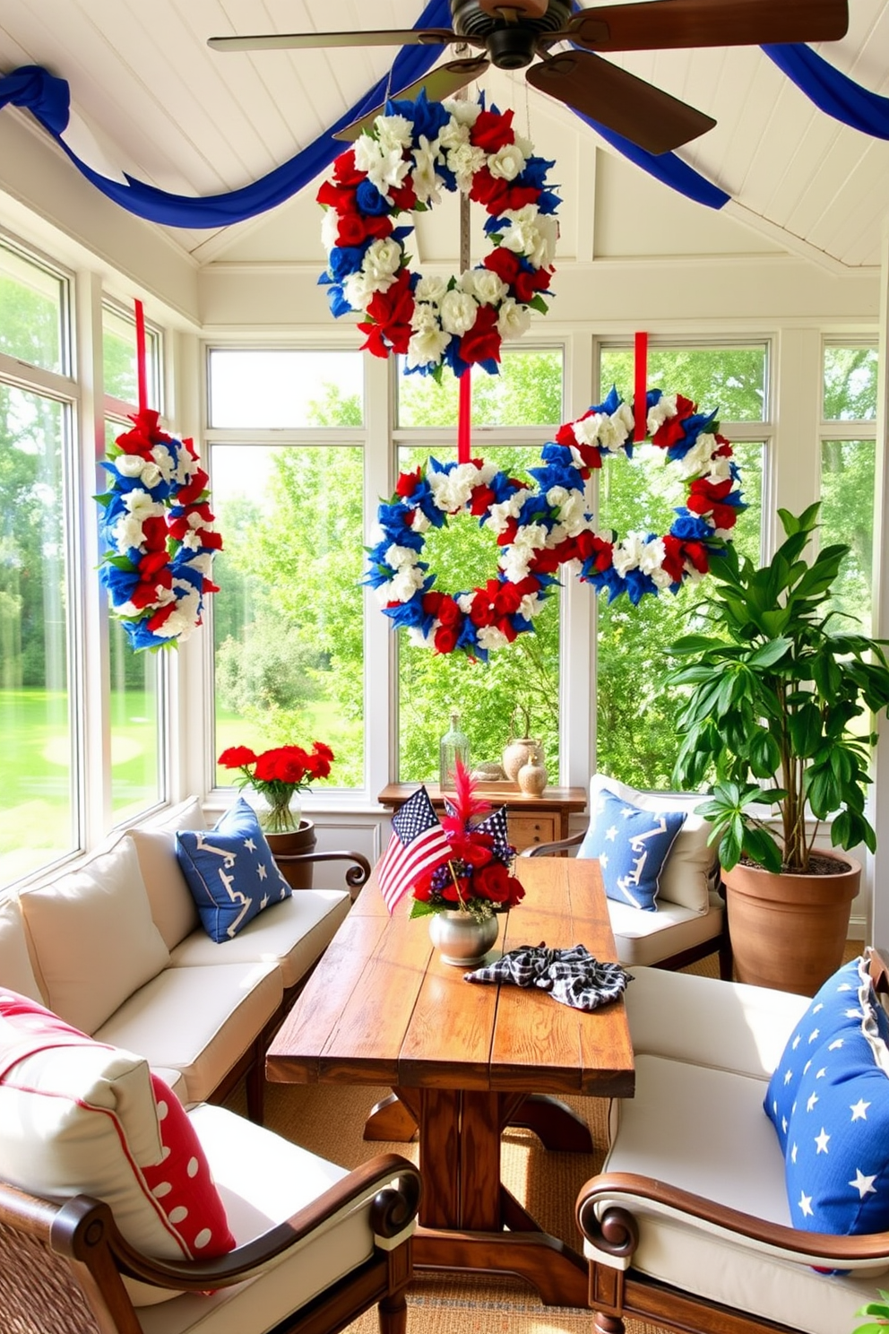 A sunroom decorated for Independence Day features a vibrant American flag themed table runner that stretches across a rustic wooden dining table. Surrounding the table are comfortable wicker chairs adorned with red and white cushions, creating a festive and inviting atmosphere.