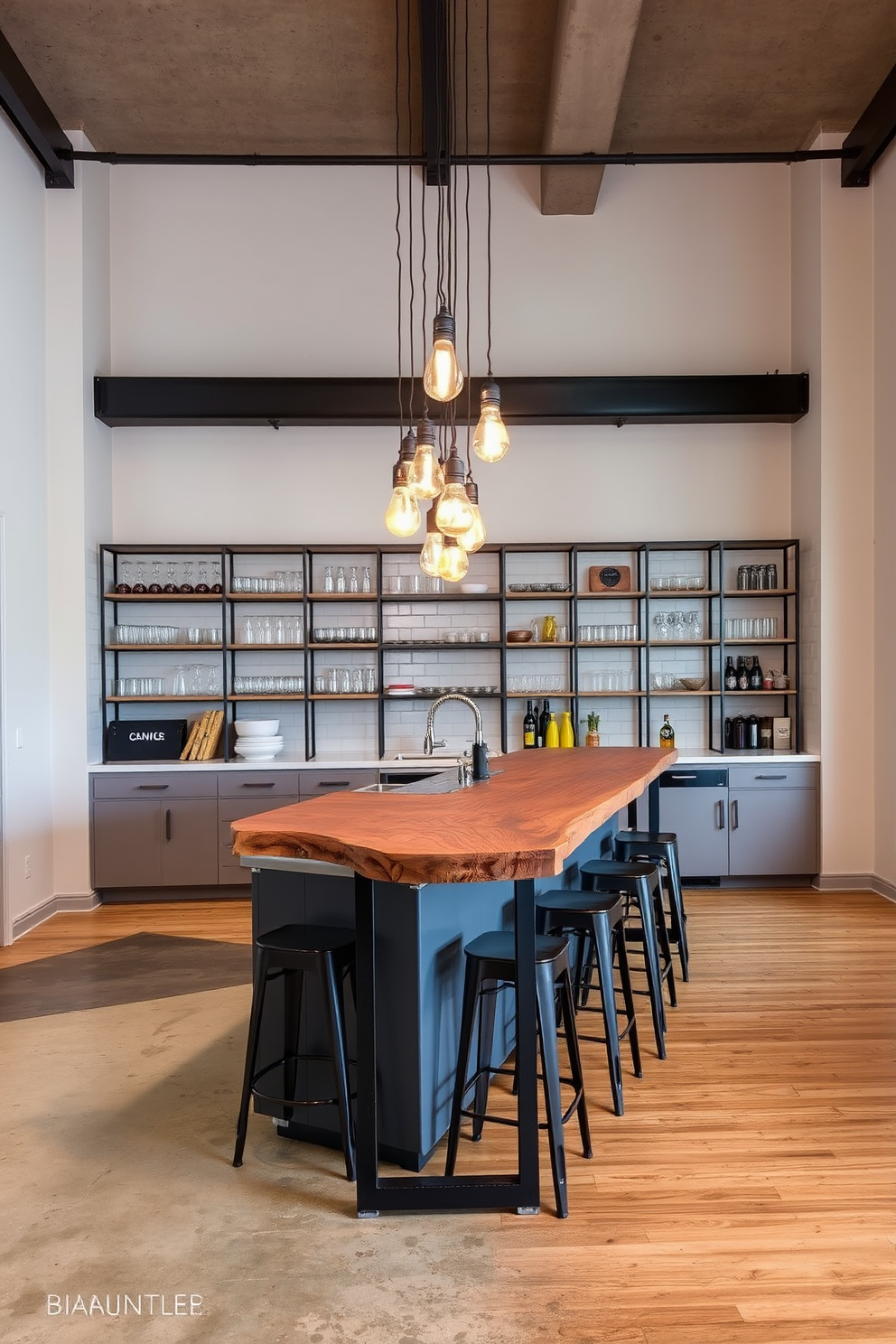 A sleek industrial kitchen bar features a long reclaimed wood countertop supported by black metal legs. Above the bar, pendant lights with exposed bulbs hang from a high ceiling, casting warm light over the space. The back wall showcases open shelving made of metal and wood, displaying an array of glassware and decorative items. A combination of concrete and hardwood flooring adds texture and warmth to the overall design.