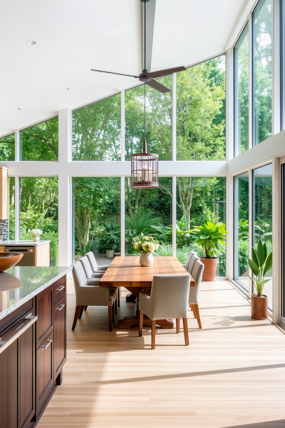 A bright and airy kitchen dining room that embraces an outdoor feel. Large floor-to-ceiling windows allow natural light to flood the space, creating a seamless connection with the lush greenery outside. The dining area features a rustic wooden table surrounded by comfortable upholstered chairs. A statement pendant light hangs above the table, adding warmth and elegance to the inviting atmosphere.