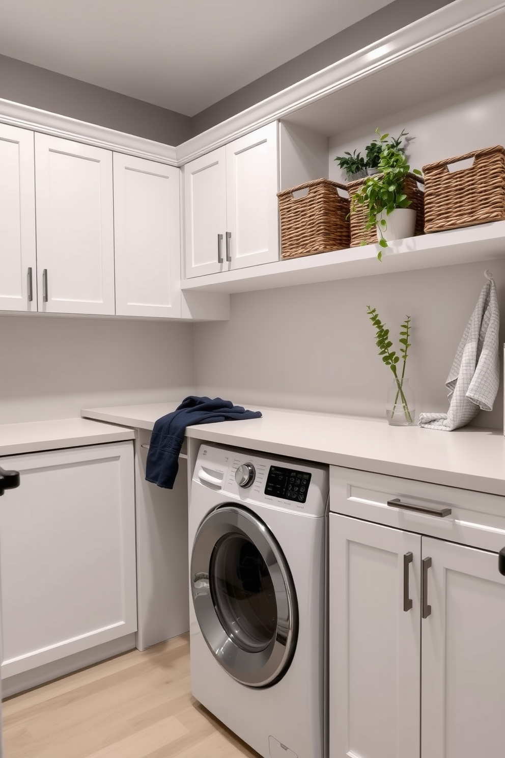 A modern laundry room featuring a spacious countertop designed for folding clothes. The cabinetry is sleek and white, with a built-in washer and dryer seamlessly integrated beneath the countertop. The walls are painted in a soft gray, creating a calm atmosphere. Stylish baskets are placed on the shelves above for organized storage, and a decorative plant adds a touch of greenery.