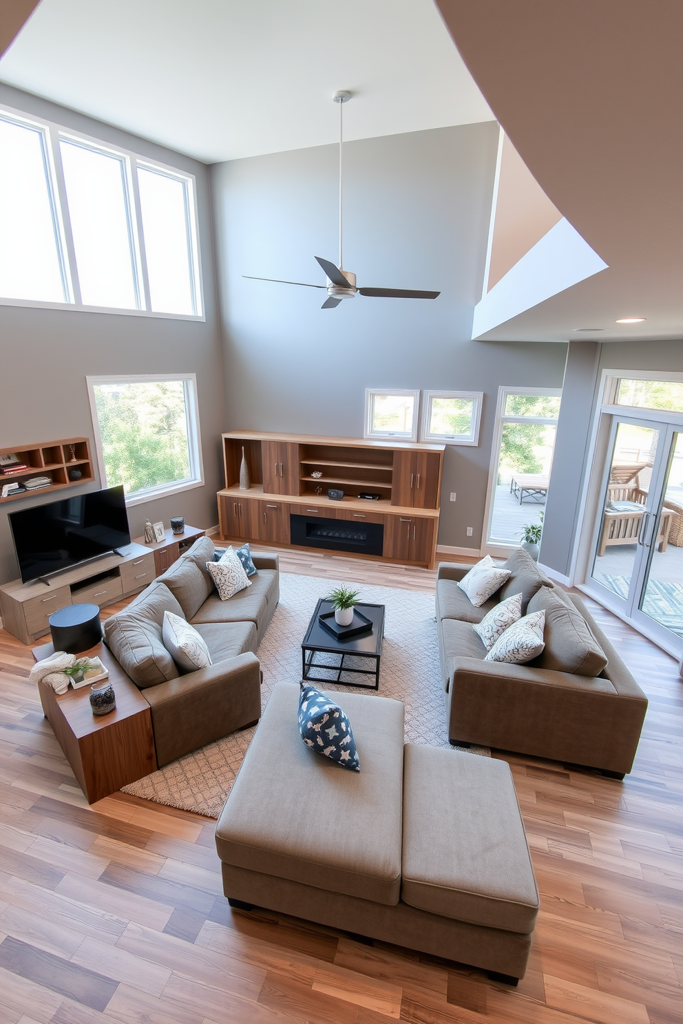 Open concept family room featuring a spacious sectional sofa positioned in the center. Large windows allow natural light to flood the space, creating an inviting atmosphere. L-shaped basement design with a cozy seating area and a modern entertainment center. The walls are painted in a soft gray, complemented by warm wooden accents throughout the room.