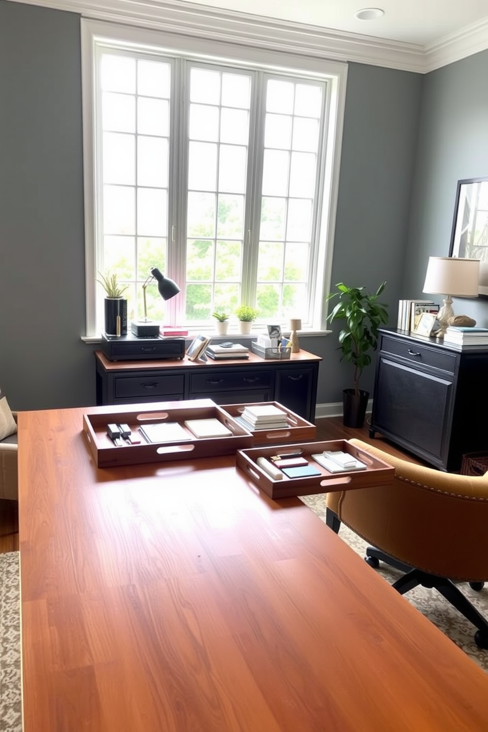 A stylish home office setup featuring a large wooden desk adorned with decorative trays for organization. The trays hold office supplies and personal items, adding a touch of elegance to the workspace. The walls are painted in a soft gray hue, complemented by a cozy armchair in a warm fabric. A large window allows natural light to flood the room, creating an inviting atmosphere perfect for productivity.