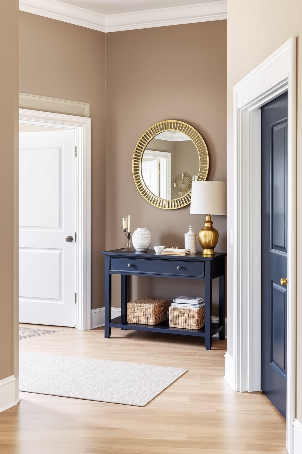 A cohesive color scheme flows throughout the entryway creating a harmonious atmosphere. The walls are painted in a soft taupe while the trim and doors are a crisp white, enhancing the spacious feel. A statement console table in a rich navy blue anchors the space, adorned with decorative items in complementary shades. A large round mirror with a gold frame hangs above the table, reflecting light and adding elegance to the design.