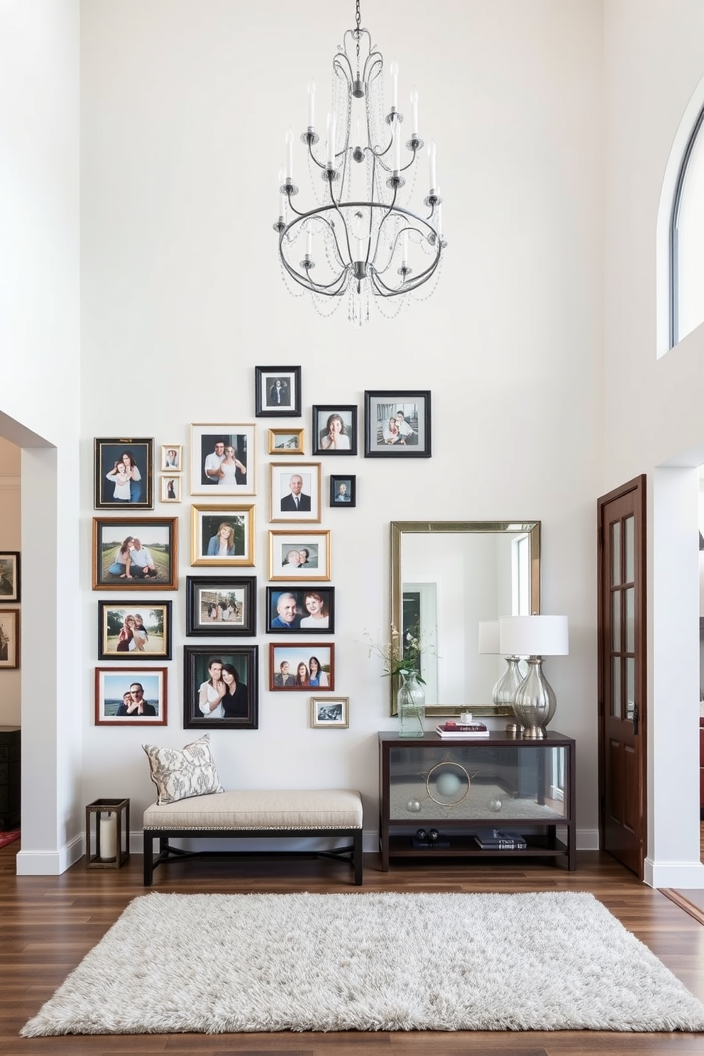 A gallery wall showcasing family photos features an arrangement of various frames in different sizes and finishes. The wall is painted in a soft white color, allowing the vibrant images to stand out, and a cozy seating area with a stylish bench sits below. The large entryway design incorporates a grand chandelier that hangs from a high ceiling, illuminating the space. A console table with decorative items and a large mirror creates an inviting focal point, complemented by a plush area rug that adds warmth underfoot.