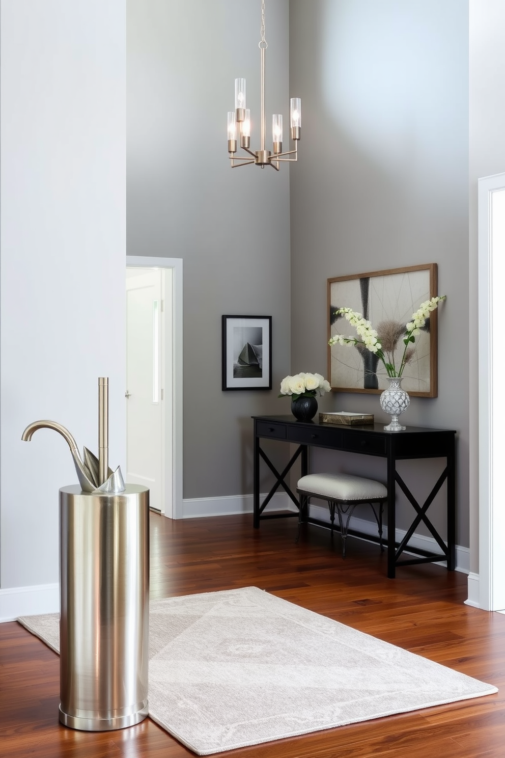 A stylish umbrella stand is positioned near the entrance, crafted from brushed metal with a sleek, modern design. The foyer features a high ceiling adorned with a statement chandelier, while the walls are painted in a soft gray, creating a welcoming atmosphere. A plush area rug in muted tones anchors the space, complementing the polished hardwood floor. Decorative wall art and a console table with fresh flowers add elegance to the overall design.