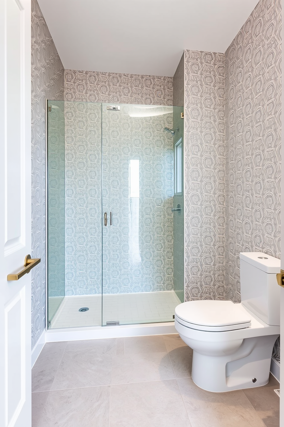 A large powder room with a sleek glass shower enclosure that creates a modern and airy feel. The walls are adorned with elegant wallpaper featuring a subtle geometric pattern, and the floor is covered with large format tiles in a soft gray tone.