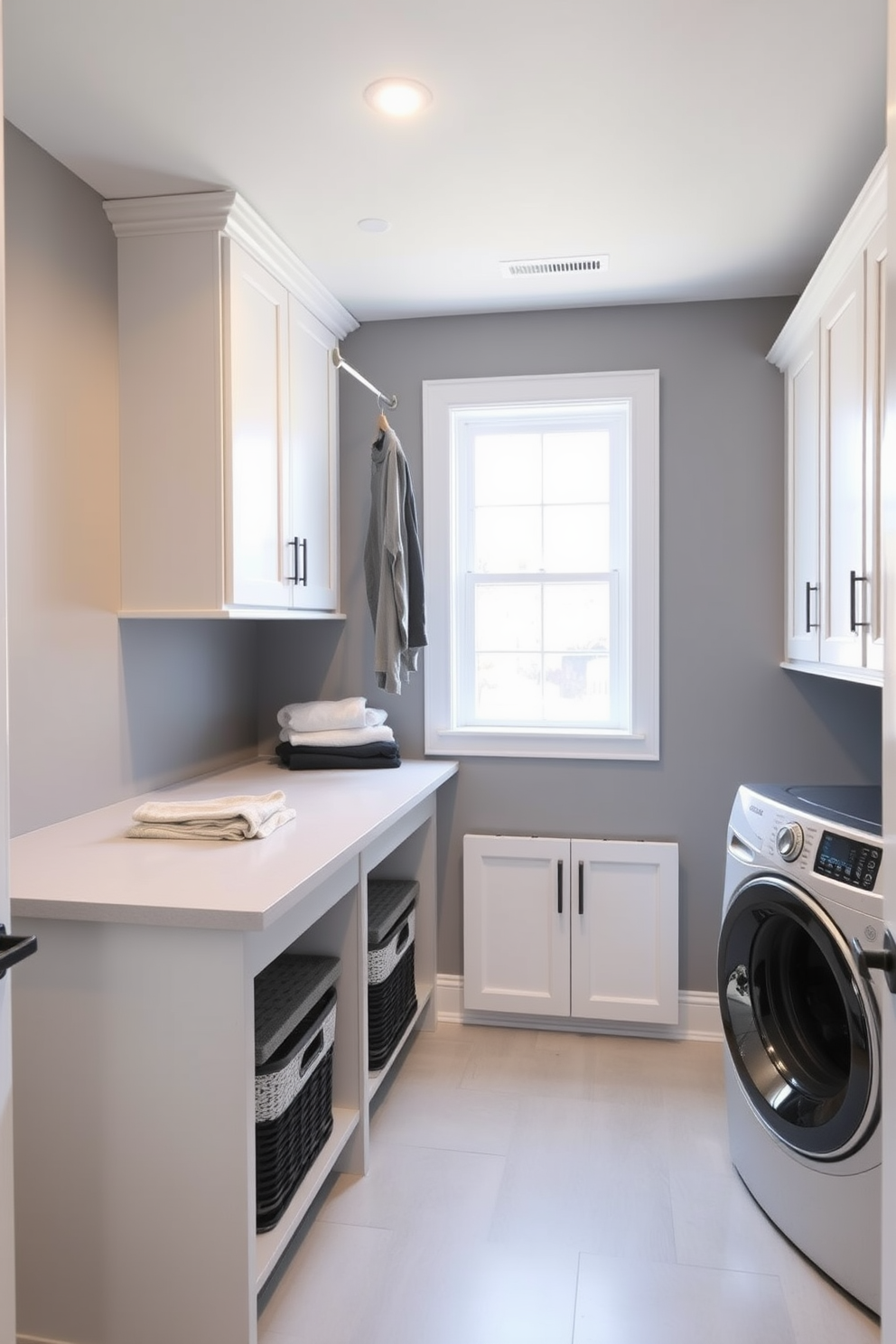 A modern laundry room in a basement featuring a spacious layout with ample natural light. There is a sleek countertop for folding clothes, and a hanging rod installed for air drying garments. The walls are painted in a soft gray hue, complemented by white cabinetry for storage. A utility sink is positioned next to the countertop, with stylish baskets underneath for organization.