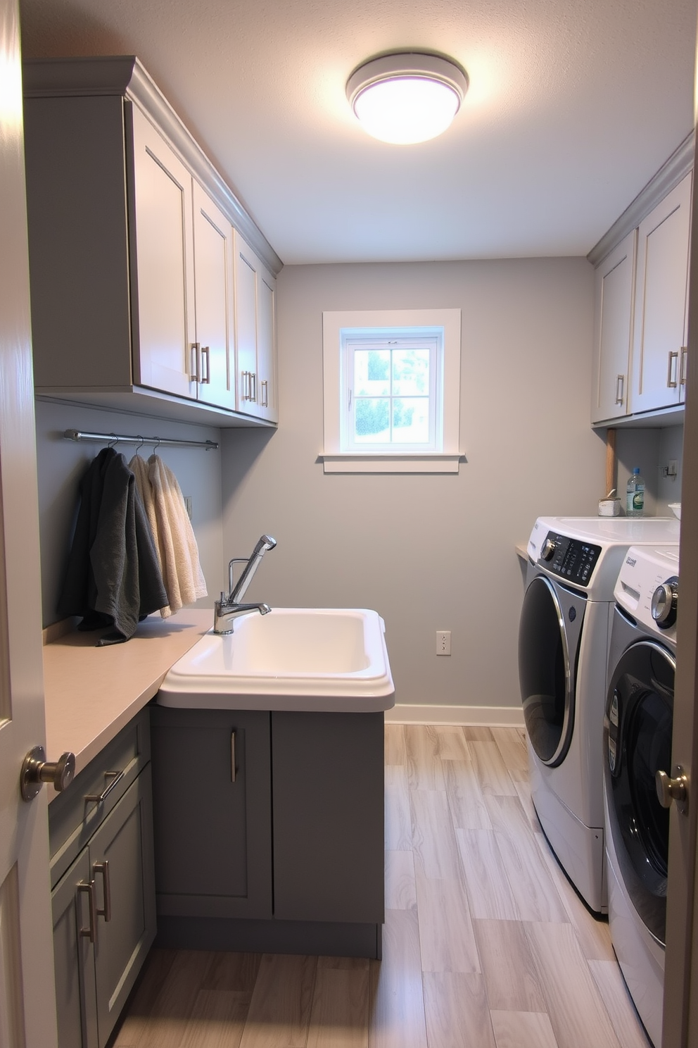 A functional laundry room in the basement features a dedicated pet washing station designed for convenience. The station includes a raised tub with a handheld showerhead, surrounded by storage cabinets for pet supplies and towels. The room is equipped with modern appliances, including a washer and dryer, set against a backdrop of light gray walls and durable vinyl flooring. Ample counter space is available for folding laundry, while a small window allows natural light to brighten the space.