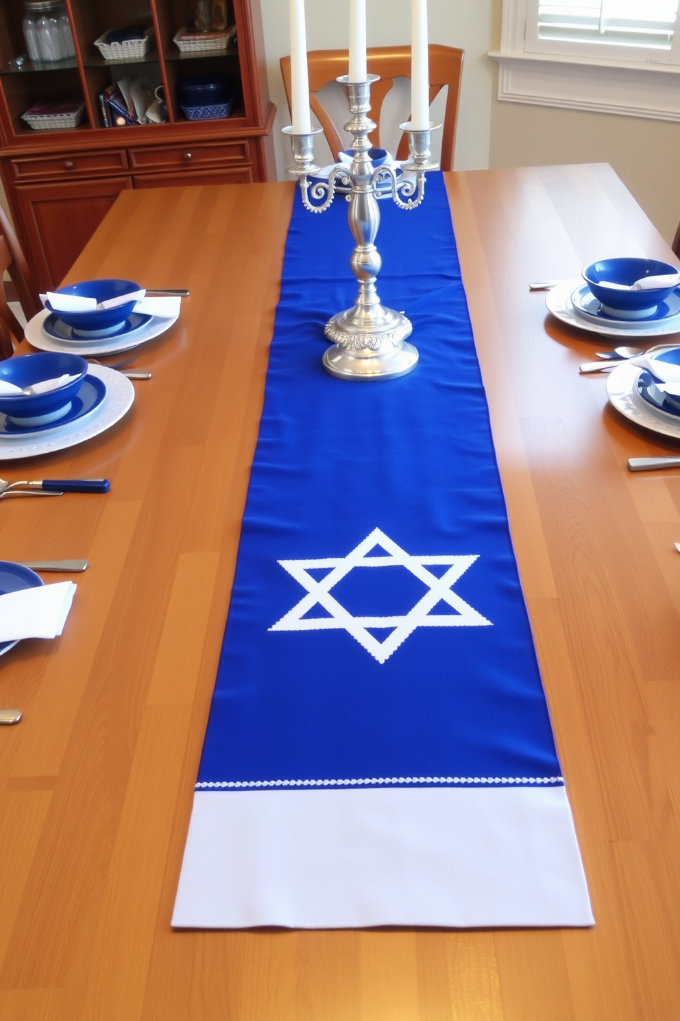 A festive table runner adorned with the Star of David stretches across a beautifully set dining table. The runner is complemented by elegant silver candle holders and blue and white dishes that enhance the Hanukkah theme.