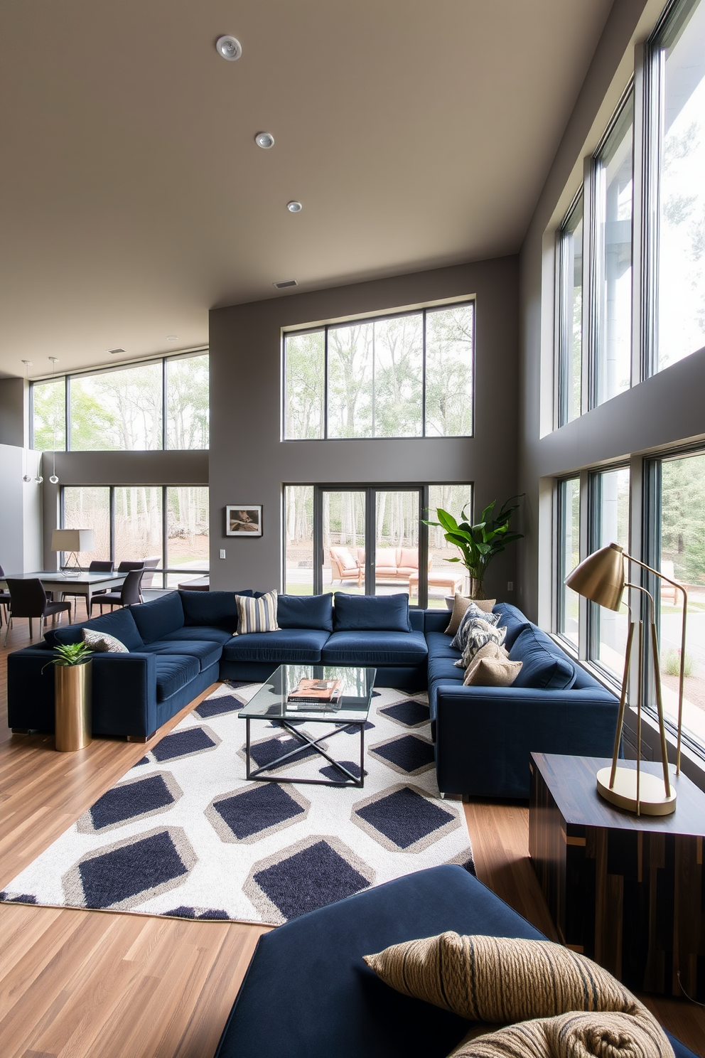 A contemporary open floor plan living room features large windows that allow natural light to flood the space. The room is furnished with a plush sectional sofa in deep navy blue, complemented by a sleek glass coffee table and a bold area rug with geometric patterns. The walls are painted in a warm gray tone, creating a cozy yet sophisticated atmosphere. Accents of dark wood and metal finishes, such as a stylish floor lamp and a media console, add a masculine touch to the overall design.