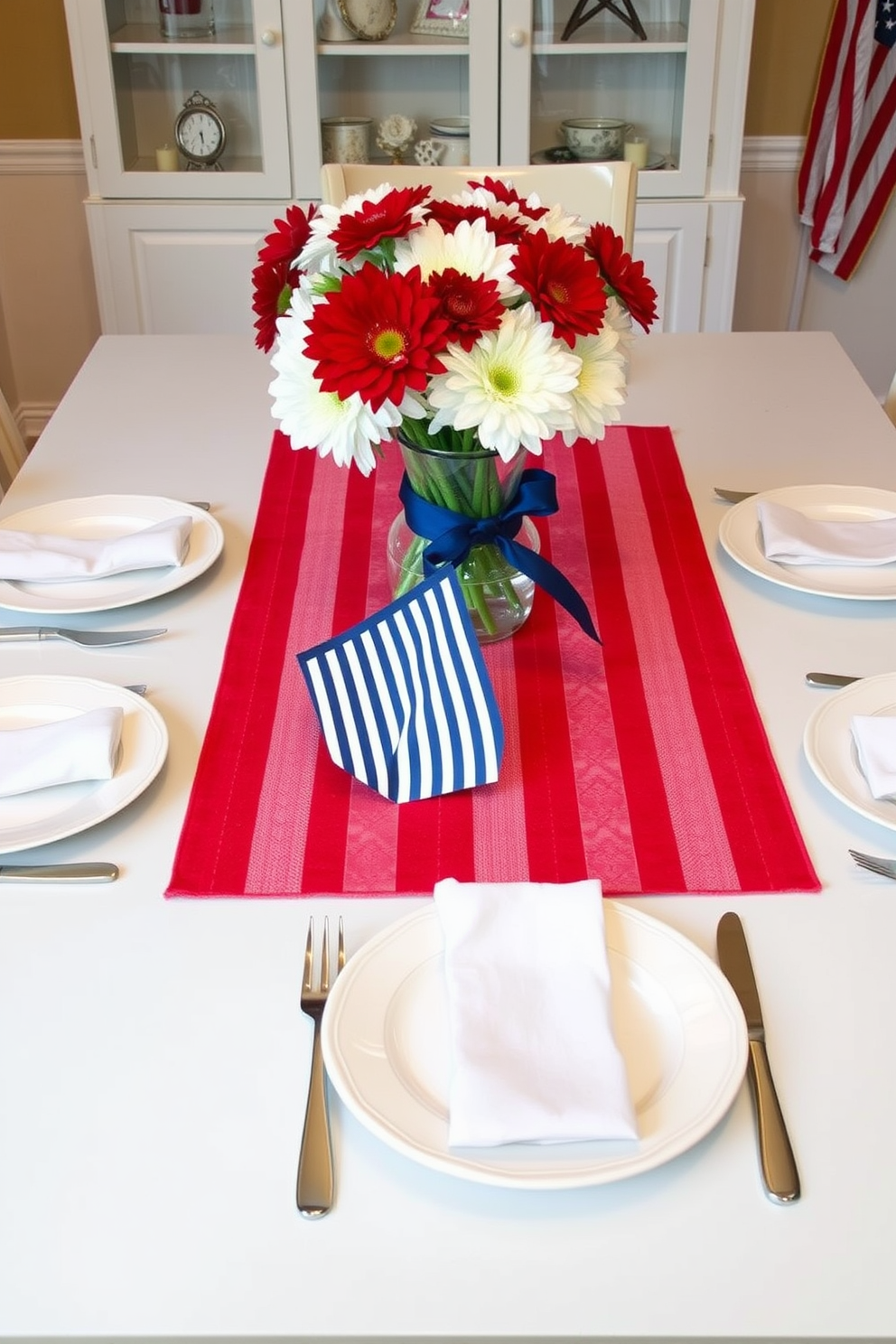 A vibrant dining table setting featuring a red striped table runner as the centerpiece. The table is adorned with white dishes and fresh flowers in a glass vase, creating a festive atmosphere for Memorial Day celebrations.