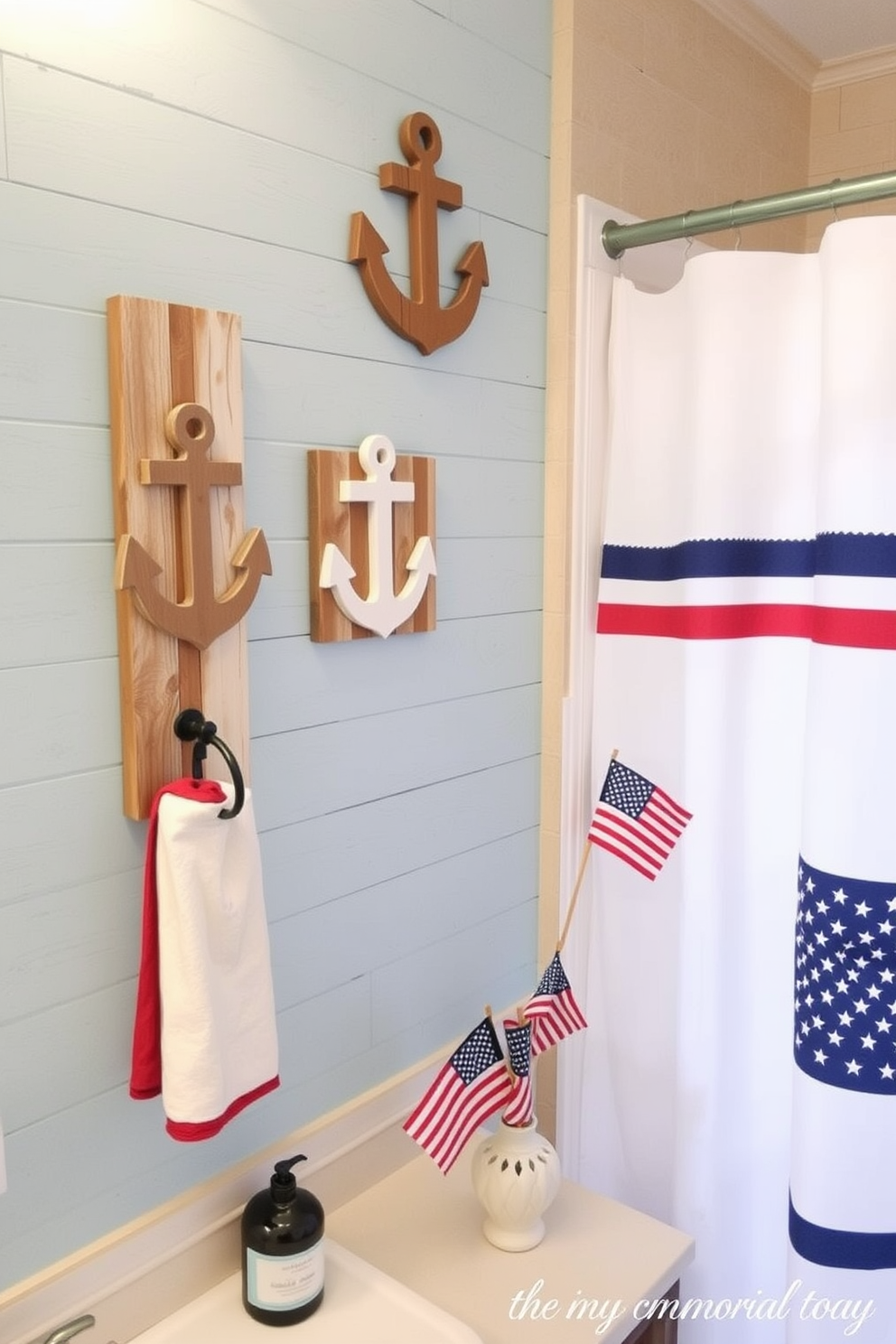 Nautical themed wall hooks are crafted from reclaimed wood and shaped like anchors and sailboats. They are mounted on a light blue shiplap wall, adding a coastal charm to the bathroom decor. For Memorial Day, the bathroom is adorned with red, white, and blue accents. A festive shower curtain displays stars and stripes, while small flags are placed in a decorative vase on the countertop.