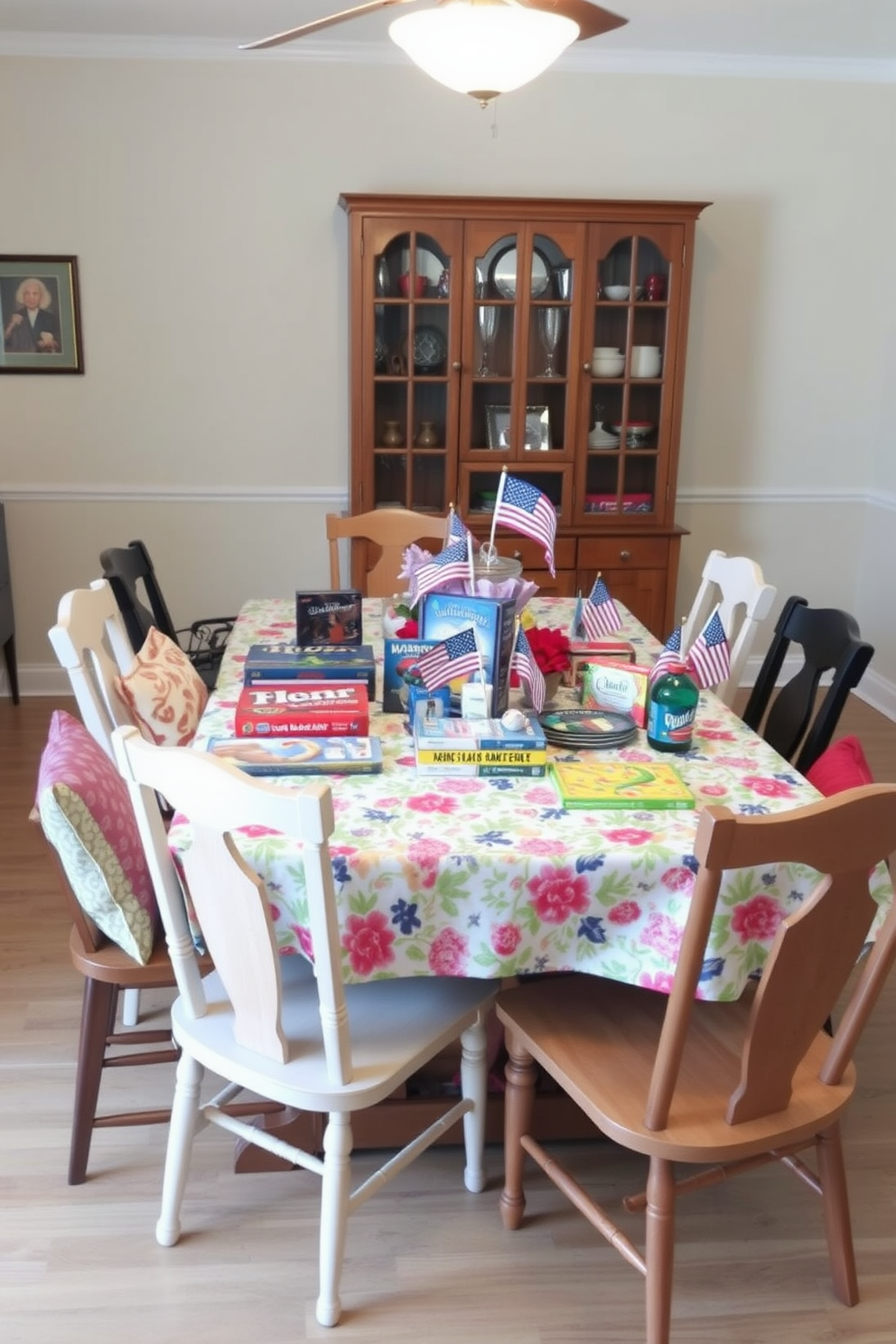 A cozy dining room setting designed for family gatherings. A large wooden table is surrounded by mismatched chairs, each with colorful cushions, creating an inviting atmosphere. The table is set with a vibrant tablecloth featuring a floral pattern. On the table, there are various tabletop games arranged alongside festive decorations for Memorial Day, including small flags and red, white, and blue accents.