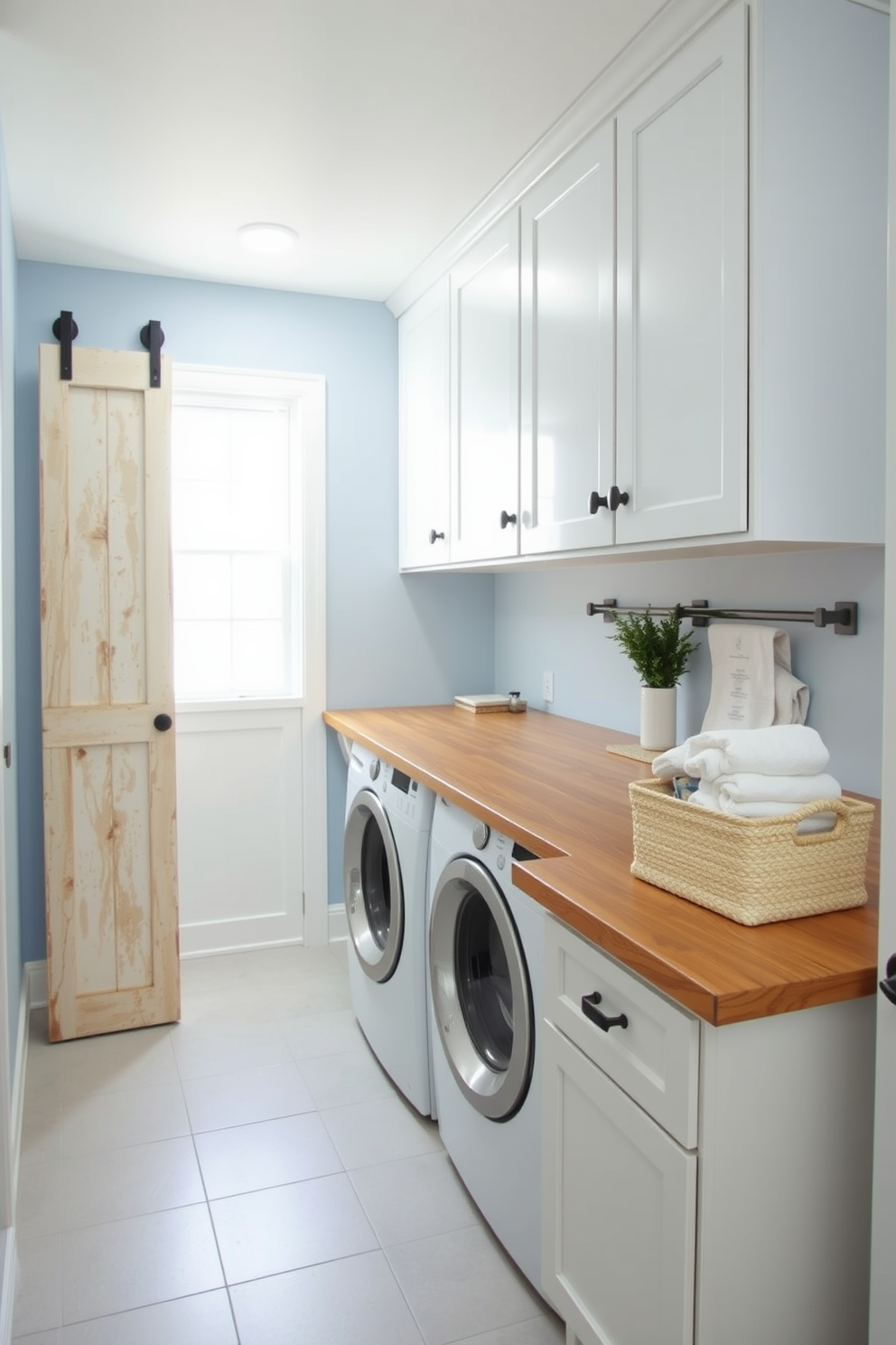 A stylish laundry room featuring a sliding barn door that adds rustic charm to the space. The walls are painted a soft blue, and the floor is covered with light gray tiles that provide a fresh and clean look. A wooden countertop holds a stack of neatly folded towels, while a decorative basket filled with laundry essentials sits nearby. Bright white cabinets above offer ample storage, and a small potted plant adds a touch of greenery to the decor.