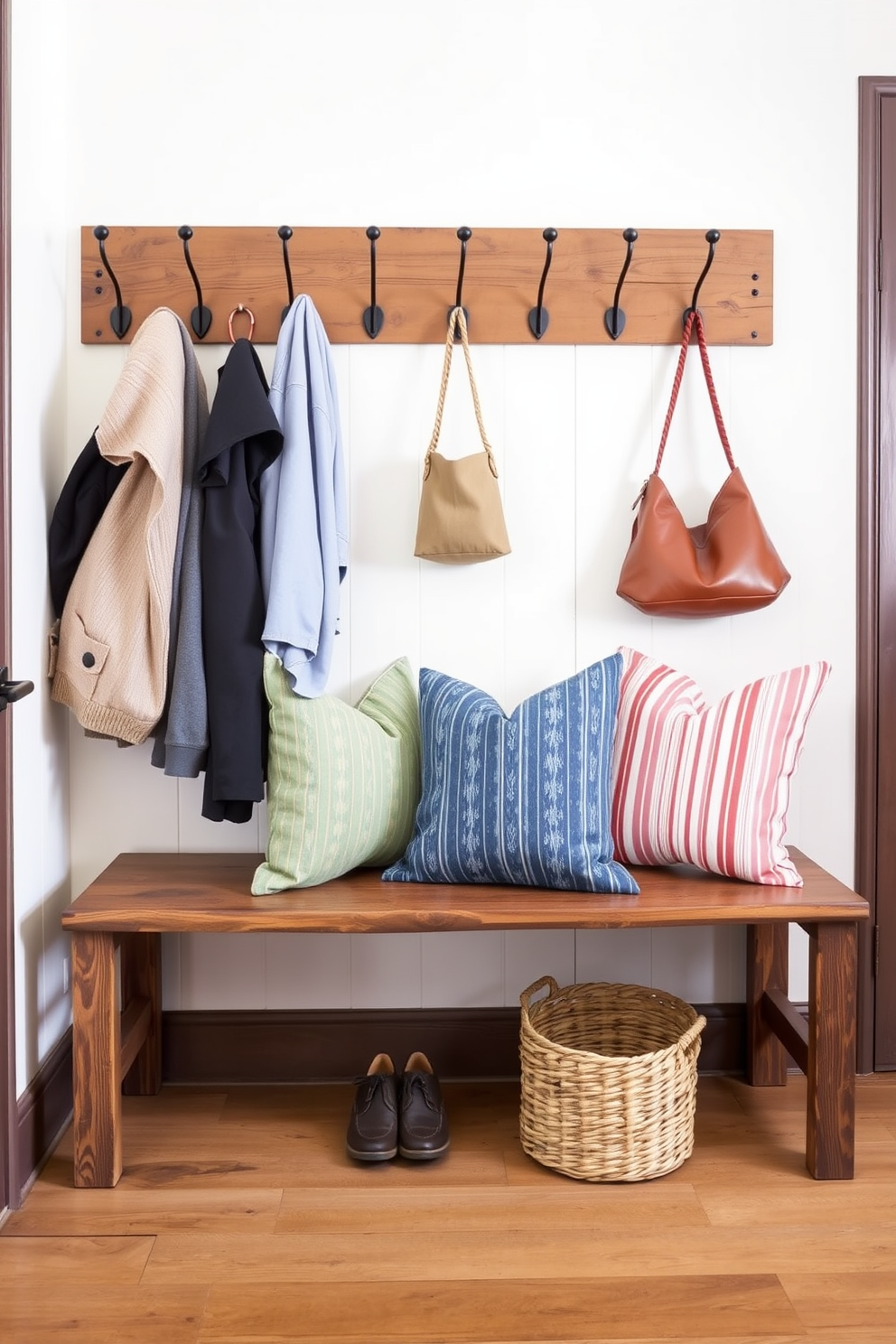 A rustic wood bench is positioned against the wall in the mudroom, adorned with soft, colorful cushions that invite comfort. Above the bench, a series of hooks are mounted for hanging jackets and bags, while a woven basket sits underneath for storing shoes.