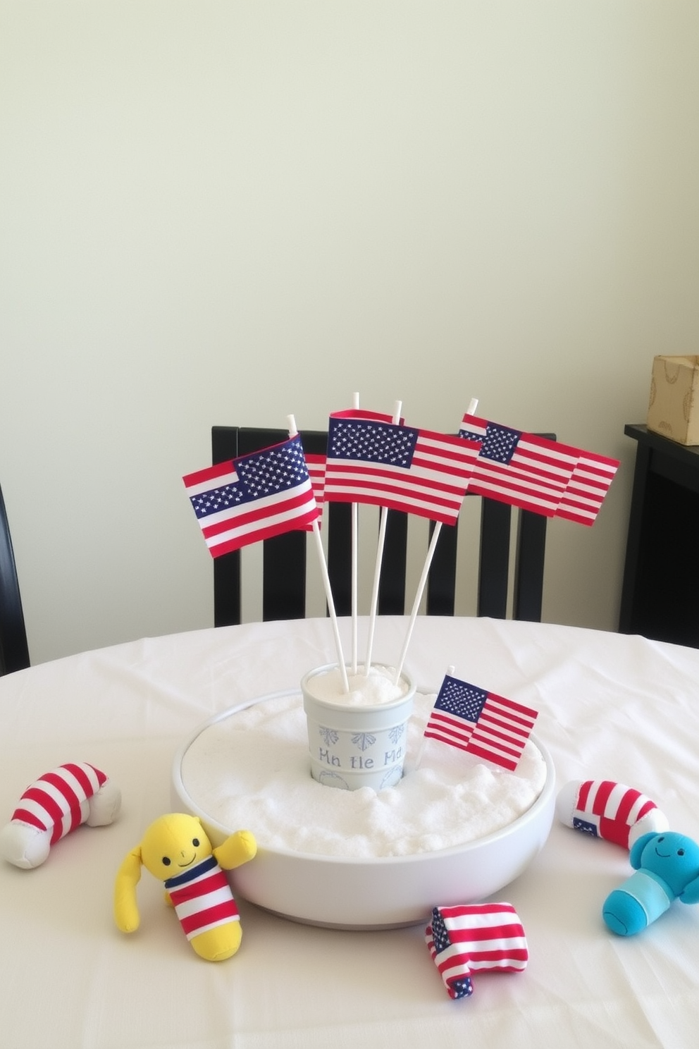 Mini flags in vibrant colors arranged as table centerpieces create a festive atmosphere for Memorial Day celebrations. Each flag is planted in a small decorative pot filled with white sand, adding a touch of beachy charm to the nursery decor. The table is adorned with a soft, pastel-colored tablecloth that complements the flags. Surrounding the centerpiece are small, plush toys in patriotic colors, enhancing the playful theme while honoring the holiday.