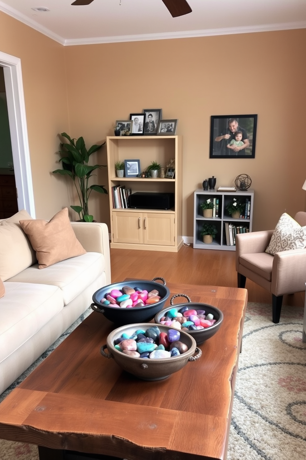 A cozy small living room adorned with decorative bowls filled with vibrant colored stones. The bowls are placed on a rustic wooden coffee table surrounded by a plush sofa and accent chairs in soft, neutral tones. The walls are painted in a warm beige, creating an inviting atmosphere. A small bookshelf in the corner displays family photos and a few potted plants, adding a personal touch to the space.