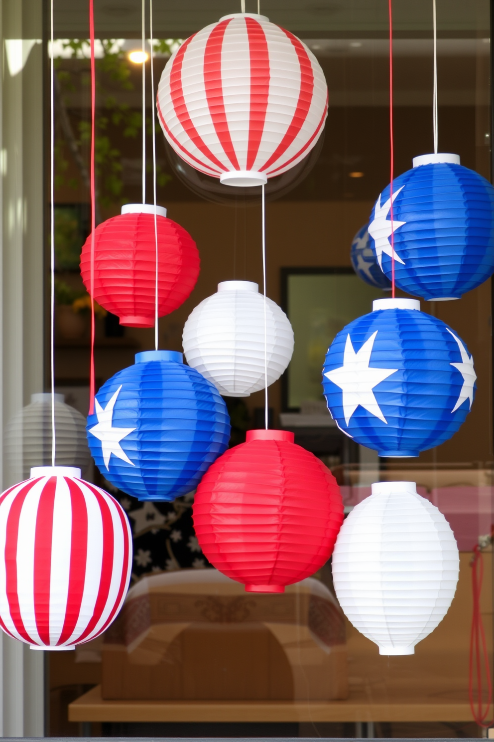 Create a festive window display featuring hanging paper lanterns in red, white, and blue to celebrate Memorial Day. The lanterns should vary in size and be arranged at different heights to create visual interest, enhancing the patriotic theme.