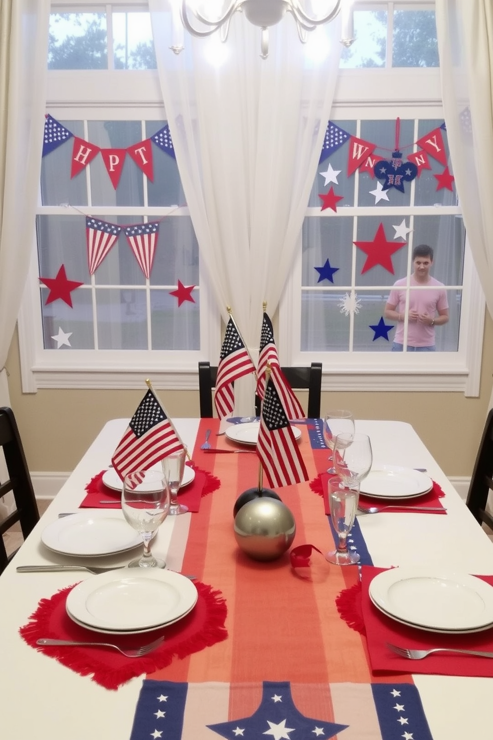 A festive dining table adorned with red white and blue table runners for Memorial Day celebrations. The table is set with white plates and sparkling glassware, while small American flags are placed in the center as a patriotic touch. Brightly colored window decorations featuring red white and blue banners and star-shaped ornaments. The windows are framed with sheer white curtains that allow natural light to illuminate the festive decor.