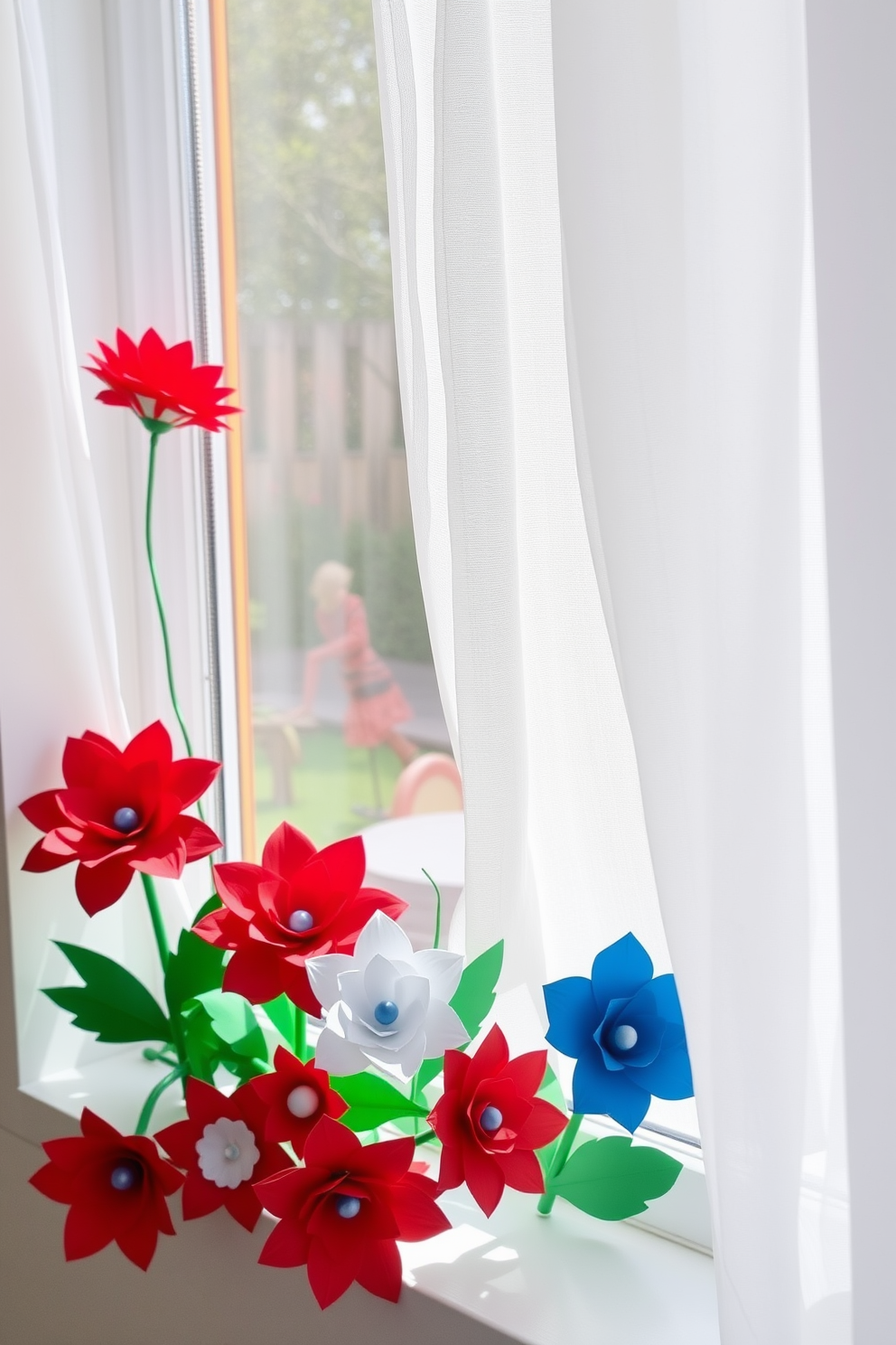 A collection of crafted paper flowers in red, white, and blue hues adorns a bright window sill. The flowers are arranged in a charming display, complemented by a backdrop of sheer white curtains that flutter gently in the breeze.