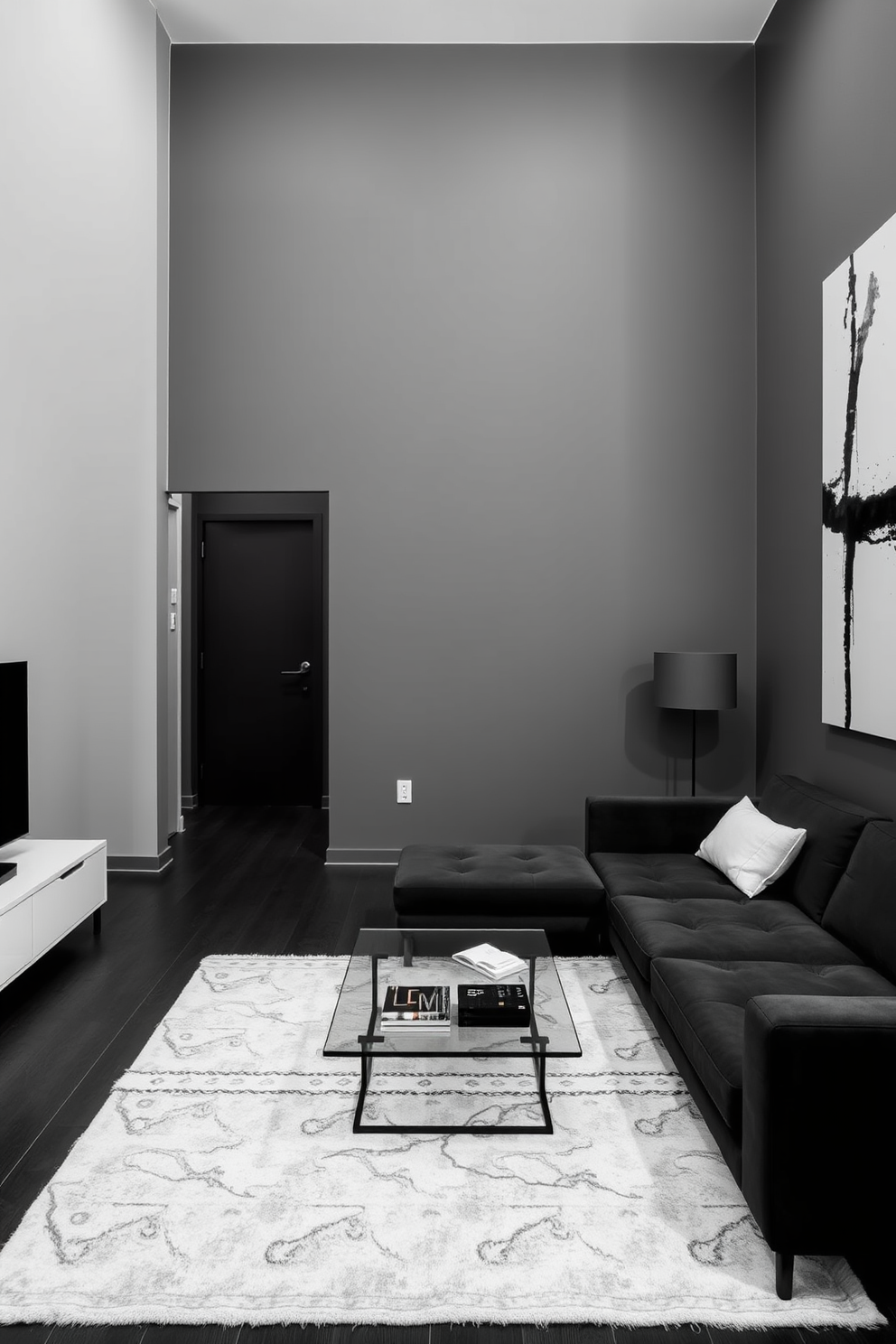 A sleek minimalist apartment featuring a monochromatic color scheme. The walls are painted in varying shades of gray, creating a cohesive and modern atmosphere. The living area includes a low-profile sofa in a charcoal hue paired with a glass coffee table. A large abstract black and white artwork adorns the wall, enhancing the contemporary feel of the space.