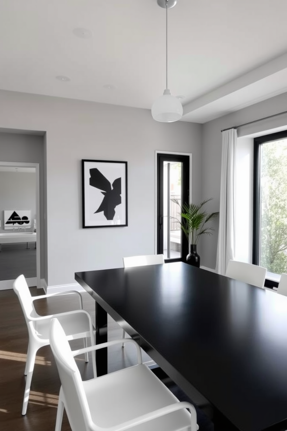 A minimalist dining room featuring a monochromatic color scheme with contrasting elements. The walls are painted in a soft gray, while the dining table is a sleek black with clean lines, surrounded by white chairs that add a striking contrast. Natural light floods the space through large windows, highlighting the simplicity of the decor. A single statement piece, such as a bold black and white artwork, hangs on the wall, drawing attention without overwhelming the room.