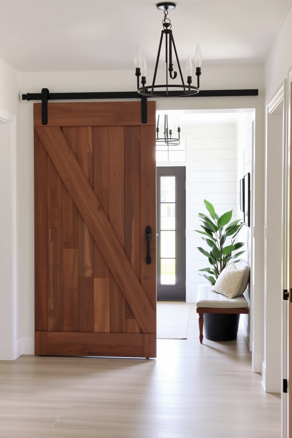 A modern farmhouse entryway features a sliding barn door made of reclaimed wood that adds rustic charm. The space is illuminated by a statement chandelier, while a cozy bench with plush cushions invites guests to sit and remove their shoes. The walls are adorned with shiplap paneling, painted in a soft white hue that enhances the natural light. A large potted plant stands in the corner, bringing a touch of greenery to the inviting atmosphere.