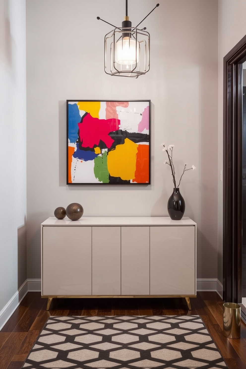 A modern entryway features a sleek console table with a glossy finish positioned against a soft gray wall. Above the table, bold abstract artwork in vibrant colors captures attention and sets the tone for the space. The floor is adorned with a stylish geometric patterned rug that adds warmth and texture. A statement light fixture hangs from the ceiling, illuminating the entryway and creating an inviting atmosphere.