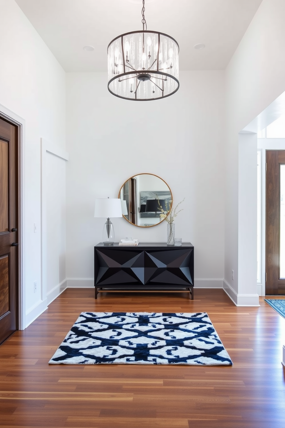 A modern foyer with statement lighting as the focal point. The entrance features a sleek console table with a geometric design, complemented by a large, eye-catching chandelier overhead. The walls are painted in a crisp white, enhancing the natural light that floods the space. A plush area rug in a bold pattern adds warmth and texture to the polished hardwood floor.