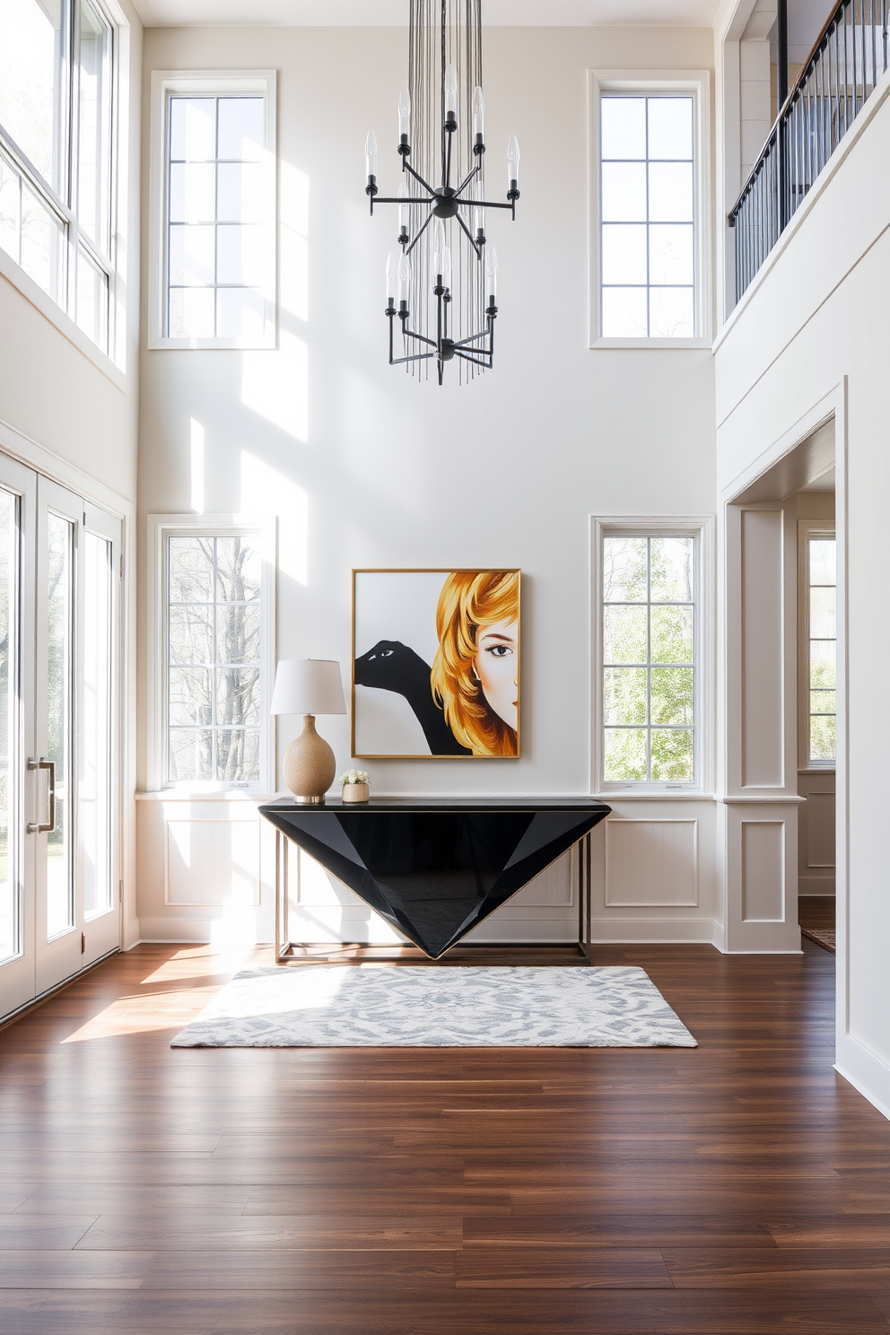 A modern foyer with high ceilings and large windows that allow natural light to flood the space. The entrance features a sleek console table with a bold geometric design and a striking piece of artwork above it. The walls are adorned with elegant wainscoting in a soft neutral tone, creating a sophisticated backdrop. A stylish area rug anchors the space, while a statement chandelier adds a touch of luxury and warmth.