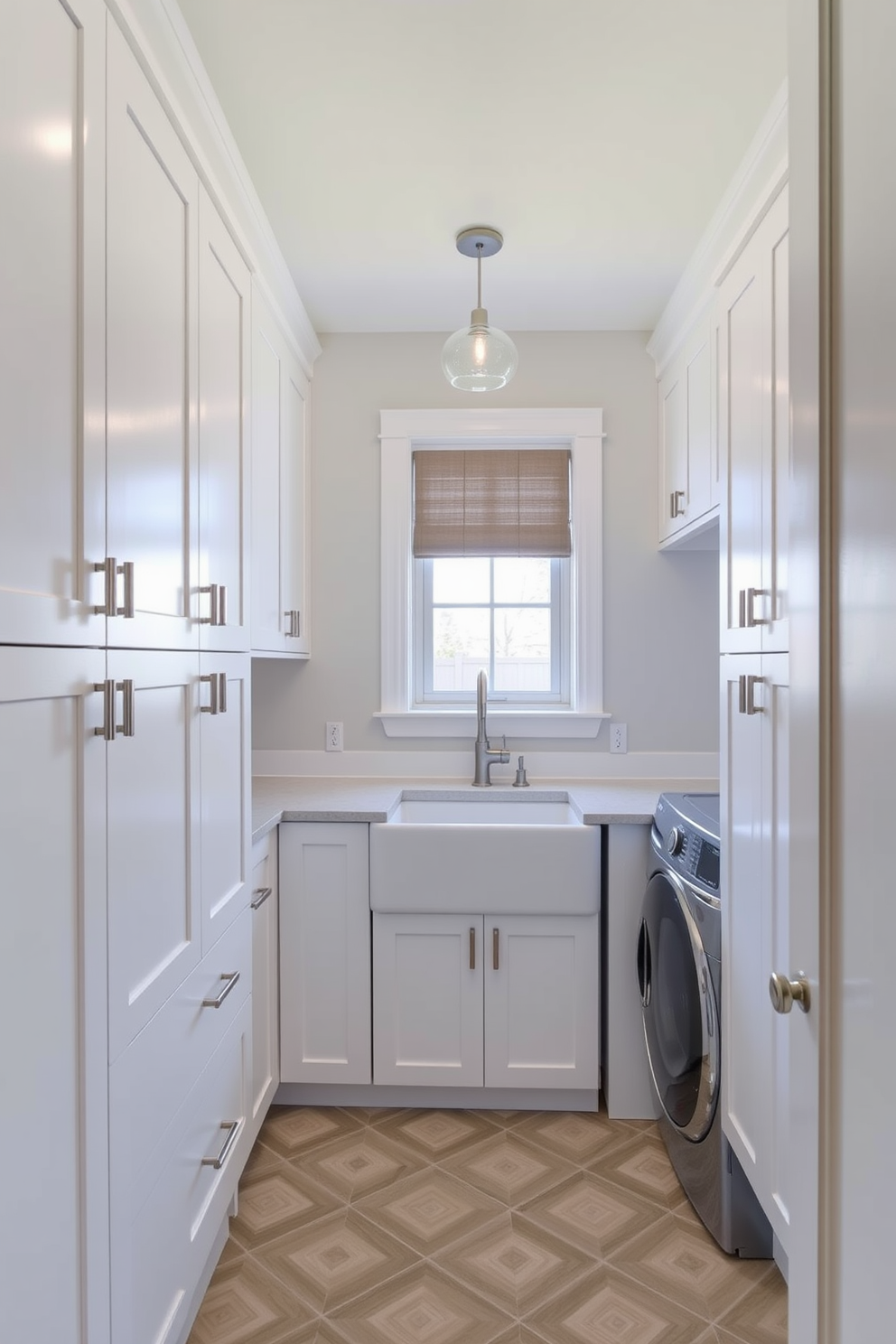 A modern laundry room features sleek cabinetry in a crisp white finish with brushed nickel handles. The room is illuminated by stylish pendant lighting that adds a chic touch above the central workspace. A large farmhouse sink sits beneath a window that lets in natural light, while a spacious countertop provides ample space for folding clothes. The floor is adorned with a geometric tile pattern that complements the overall design aesthetic.