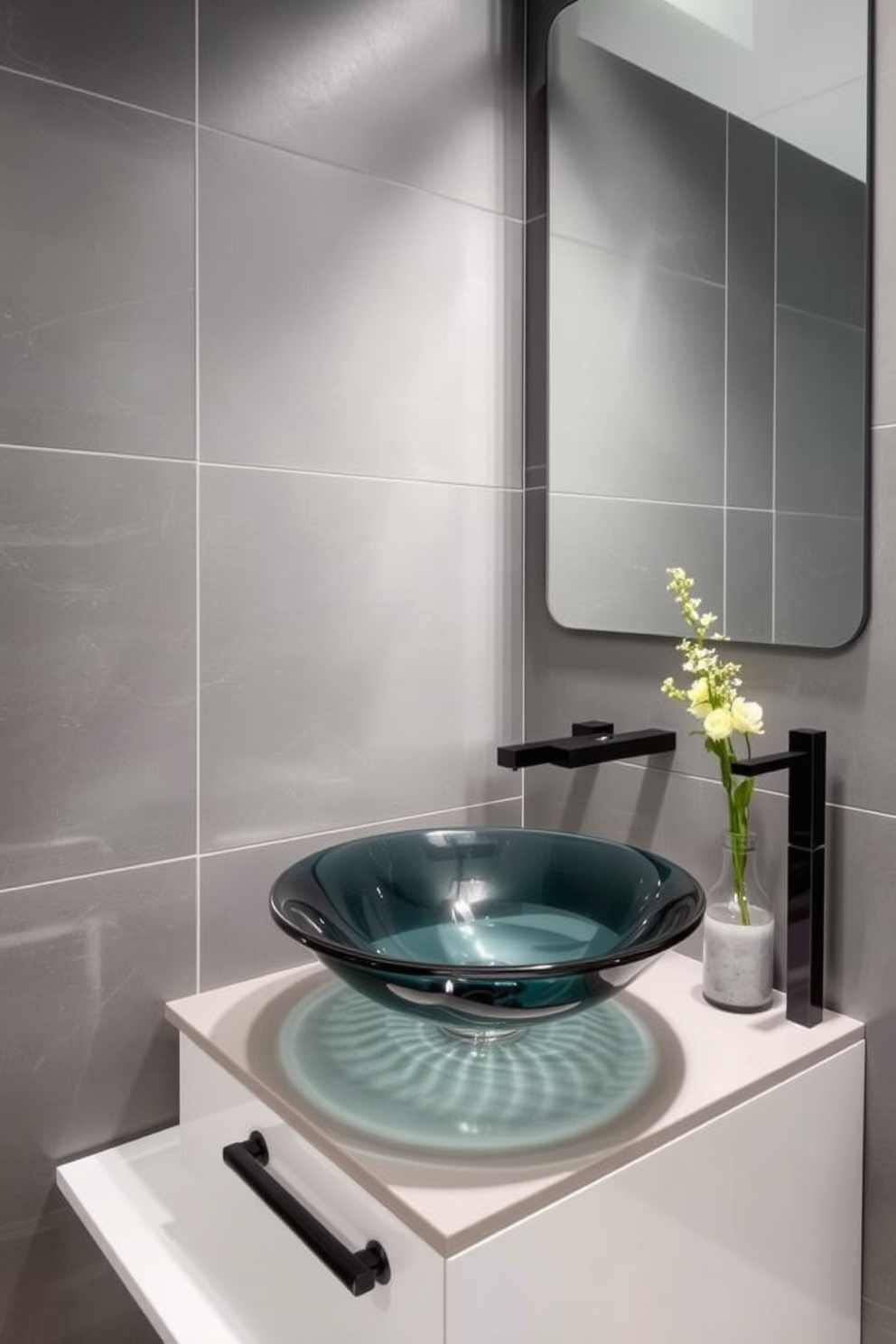 A modern powder room featuring a unique vessel sink made of hand-blown glass. The walls are adorned with sleek gray tiles and complemented by a stylish floating vanity with minimalist hardware.